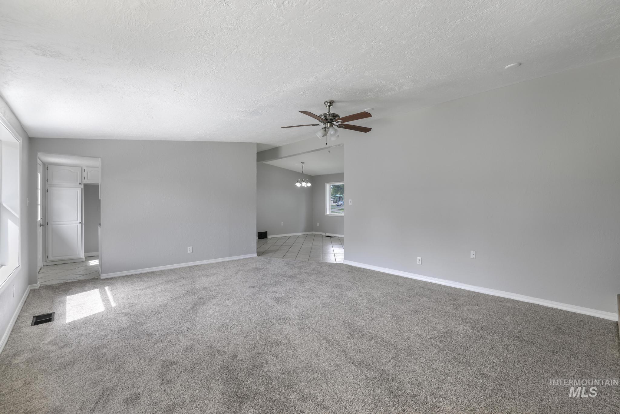 Unfurnished room with light colored carpet, a chandelier, a textured ceiling, and a ceiling fan