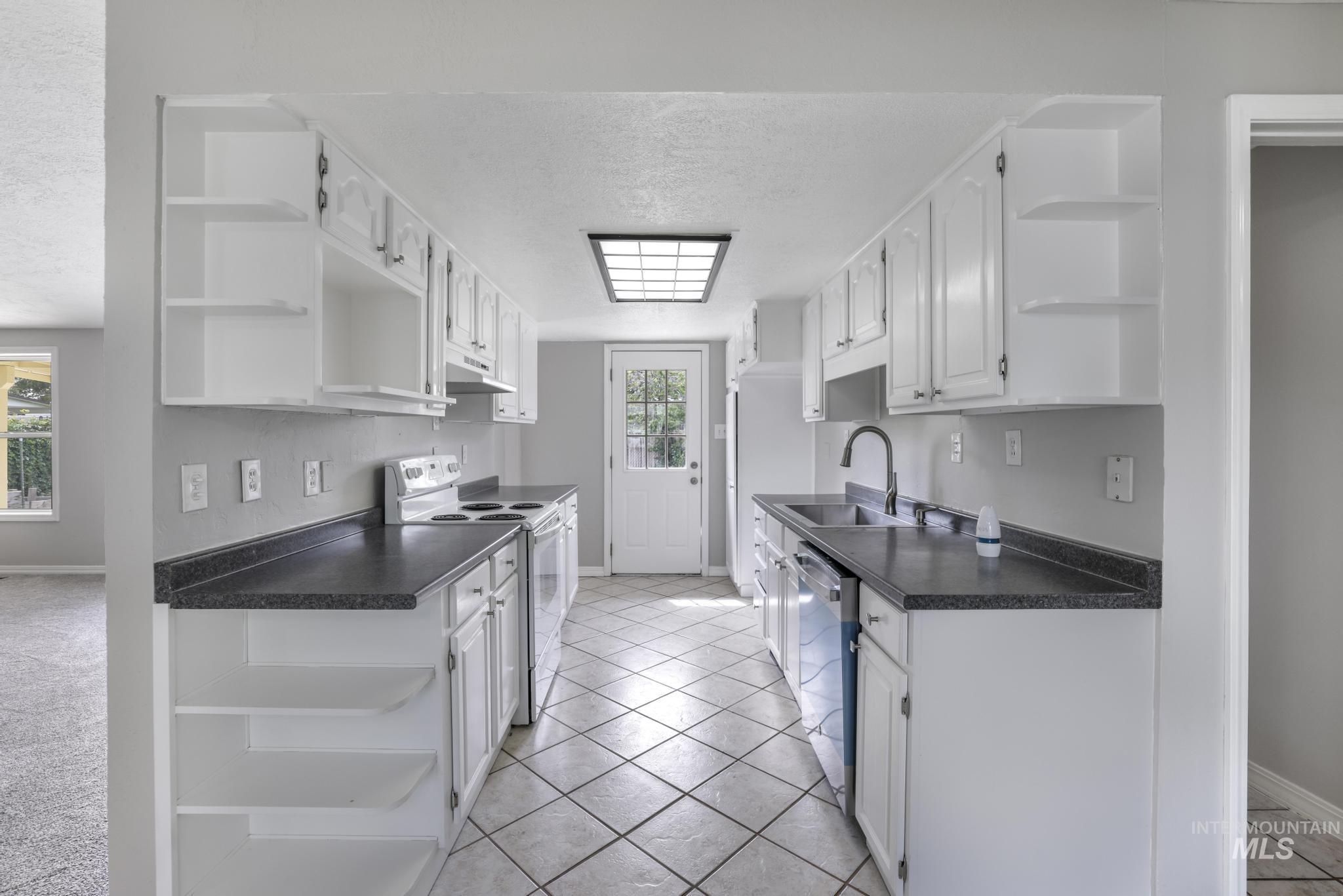 Kitchen featuring open shelves, white electric stove, dark countertops, light tile patterned floors, and a textured ceiling