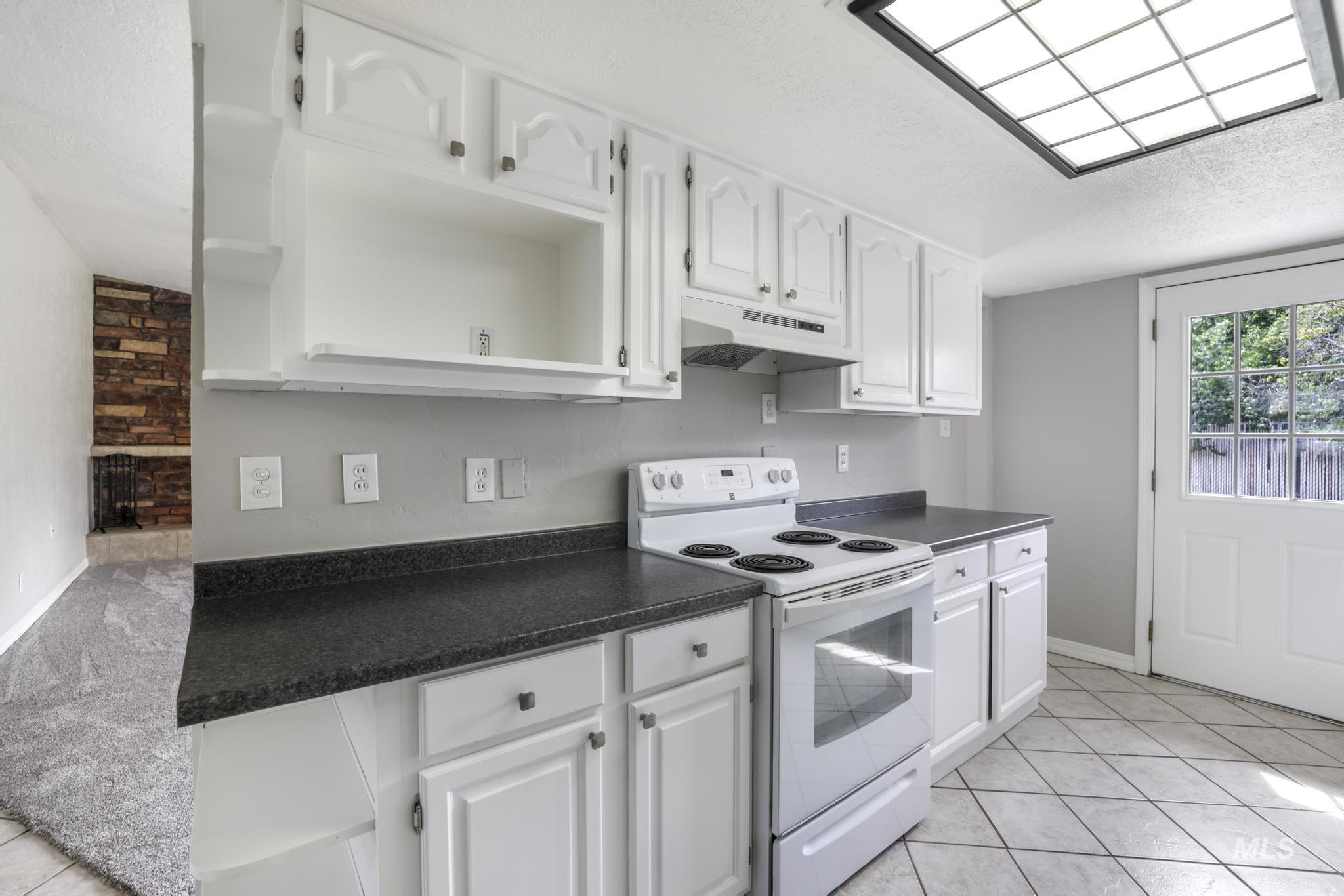 Kitchen with white electric range, open shelves, dark countertops, light tile patterned floors, and white cabinets
