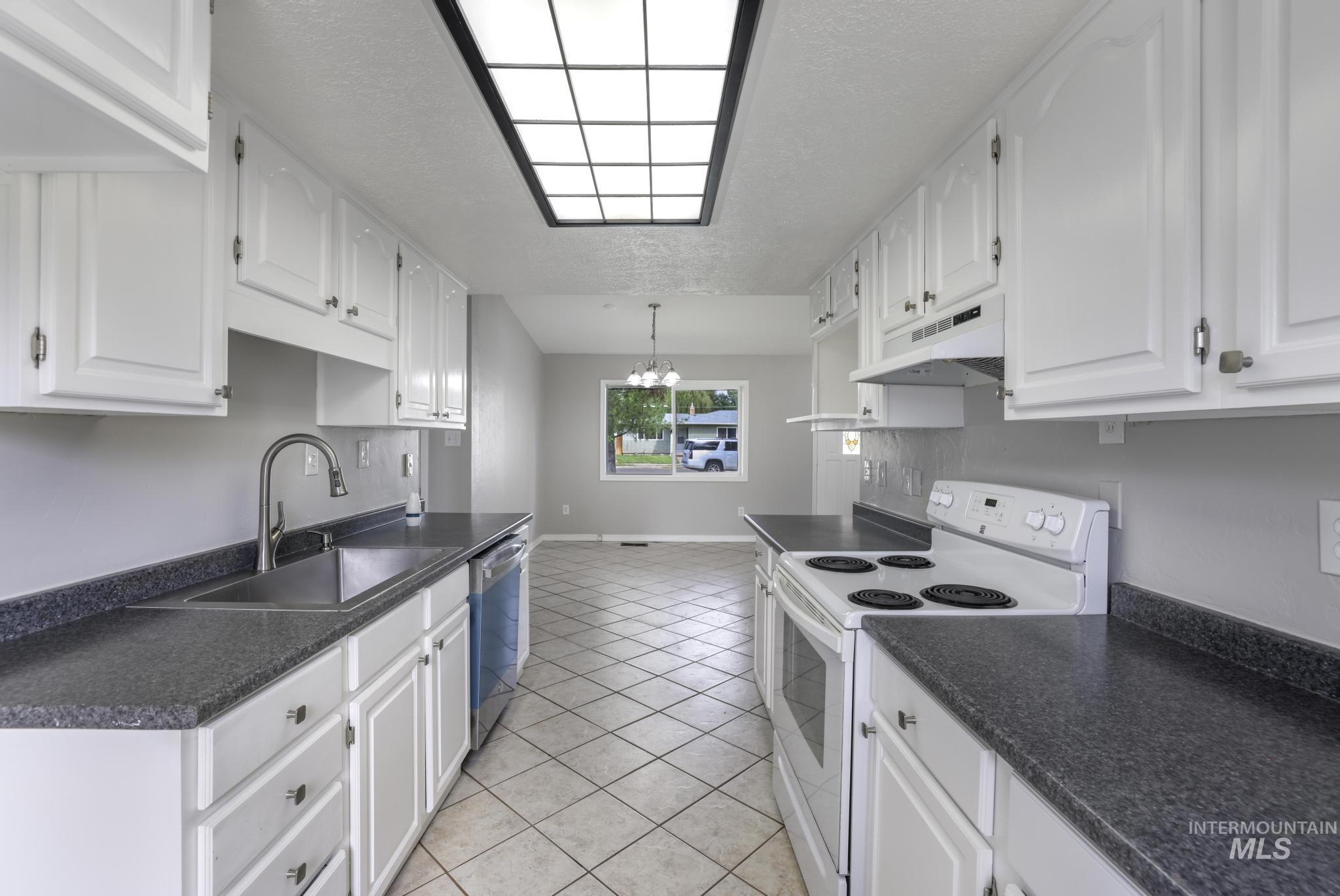 Kitchen featuring white range with electric cooktop, dark countertops, white cabinets, hanging light fixtures, and a textured ceiling