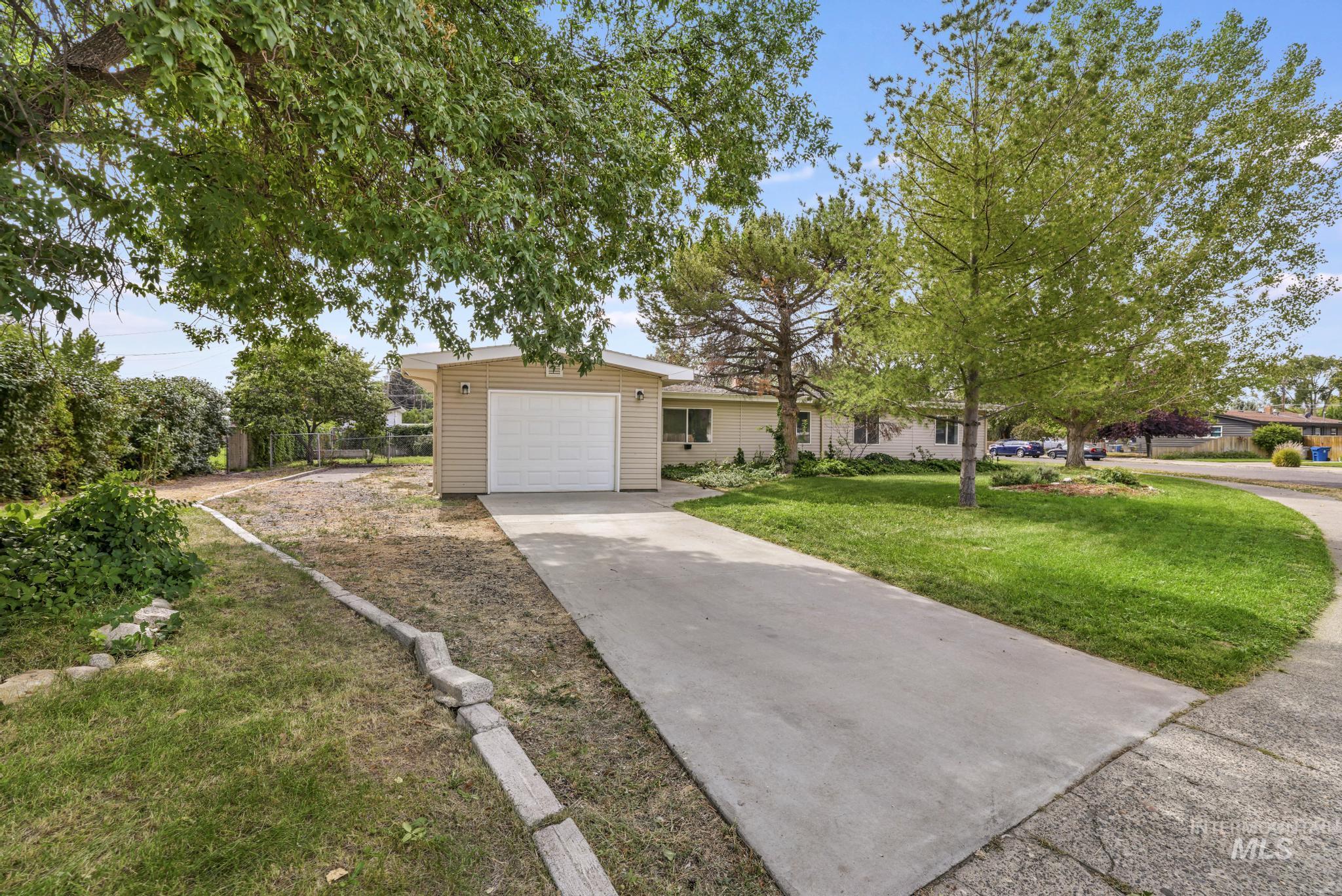 Ranch-style home featuring concrete driveway, an attached garage, and a front lawn