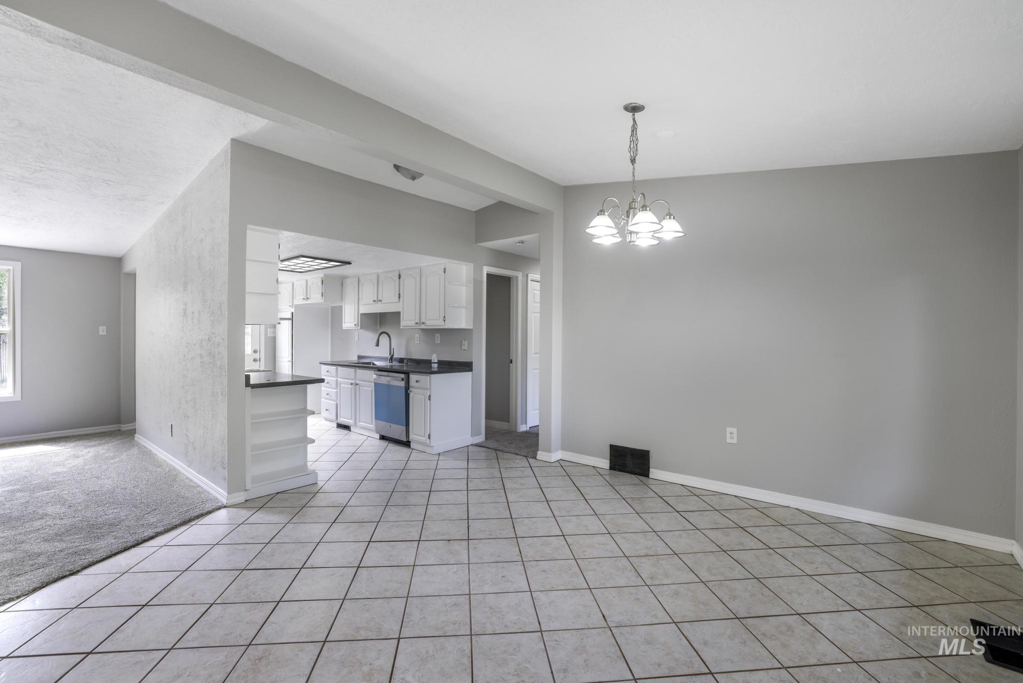 Kitchen with dark countertops, light tile patterned floors, white cabinetry, and a chandelier