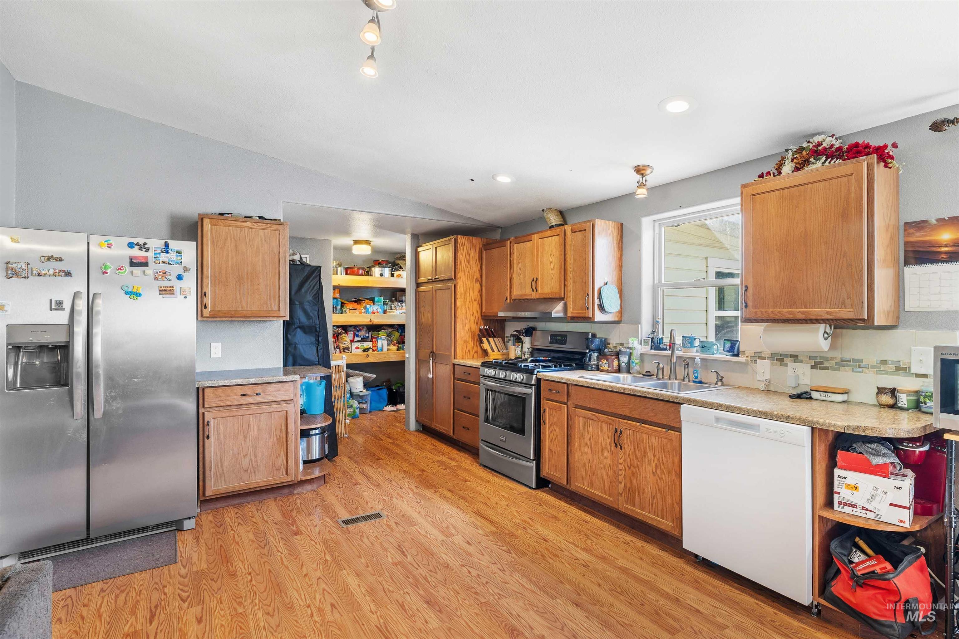 Kitchen featuring stainless steel appliances, vaulted ceiling, light countertops, light wood-style flooring, and brown cabinetry