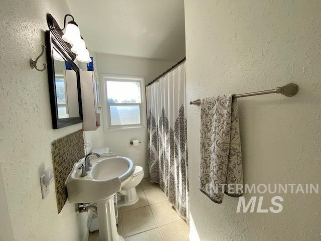 Full bath with a textured wall, light tile patterned floors, and curtained shower