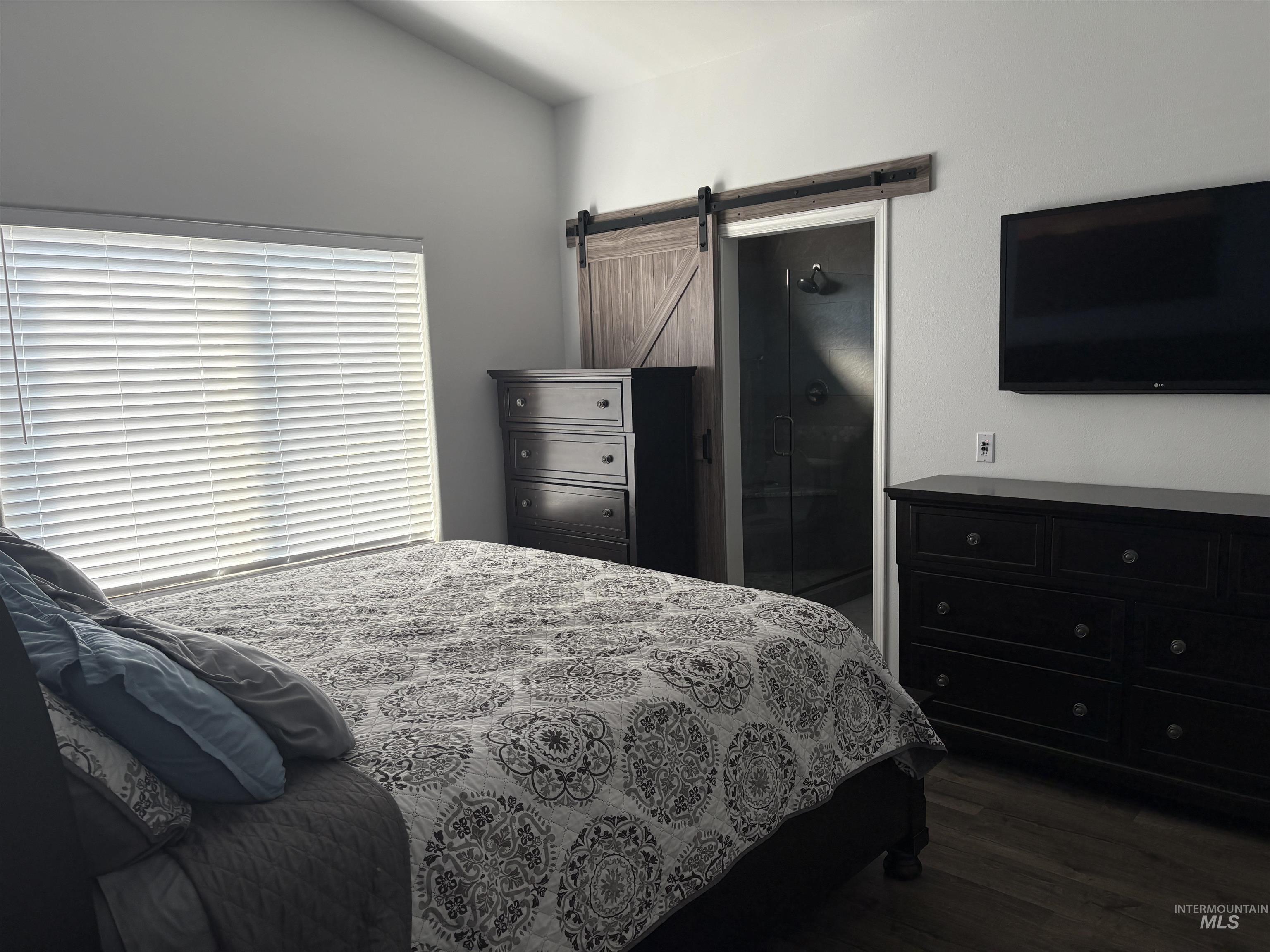 Bedroom with a barn door, dark wood-type flooring, and vaulted ceiling