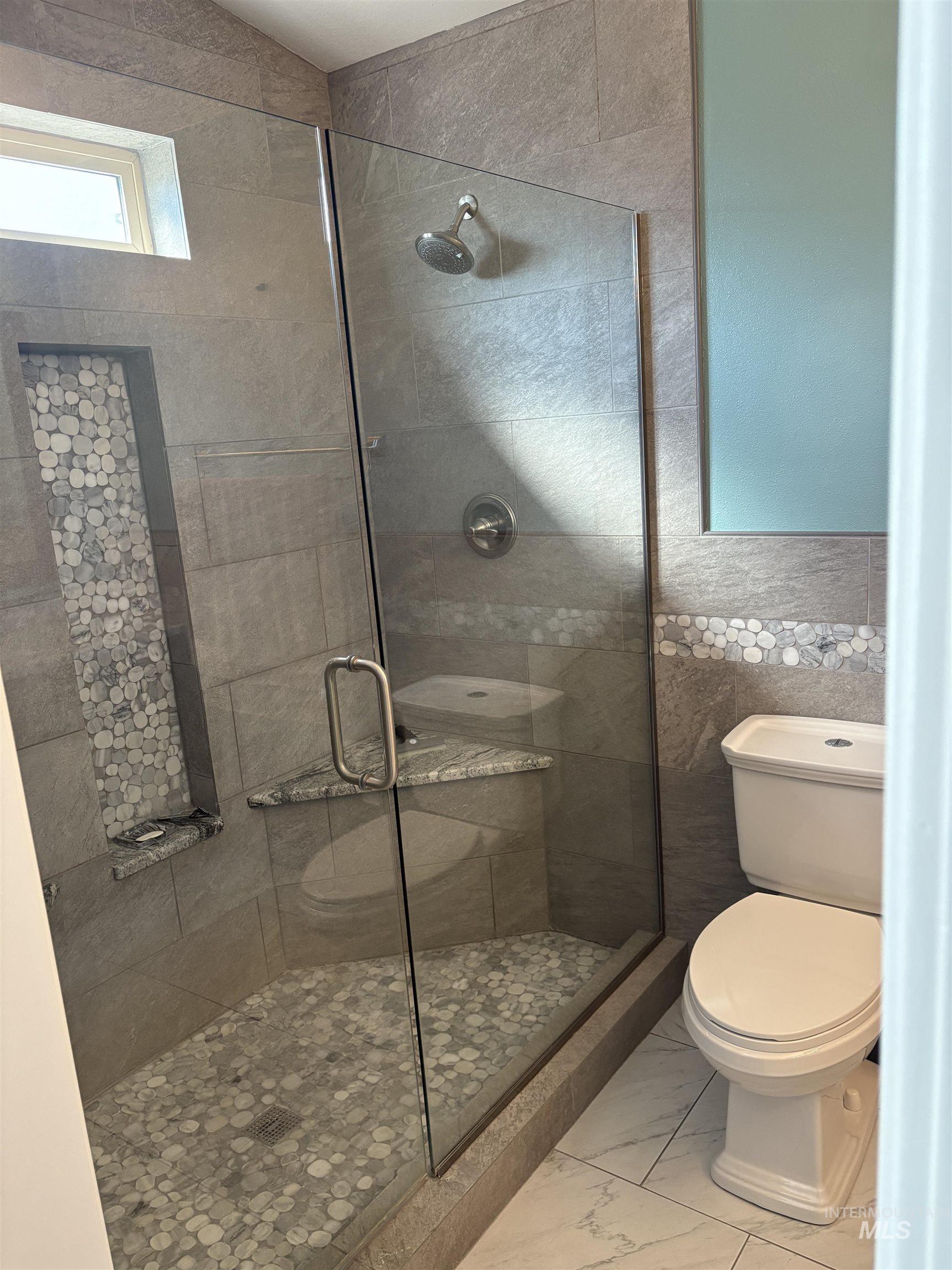 Full bathroom featuring a stall shower, light marble finish floors, and tile walls