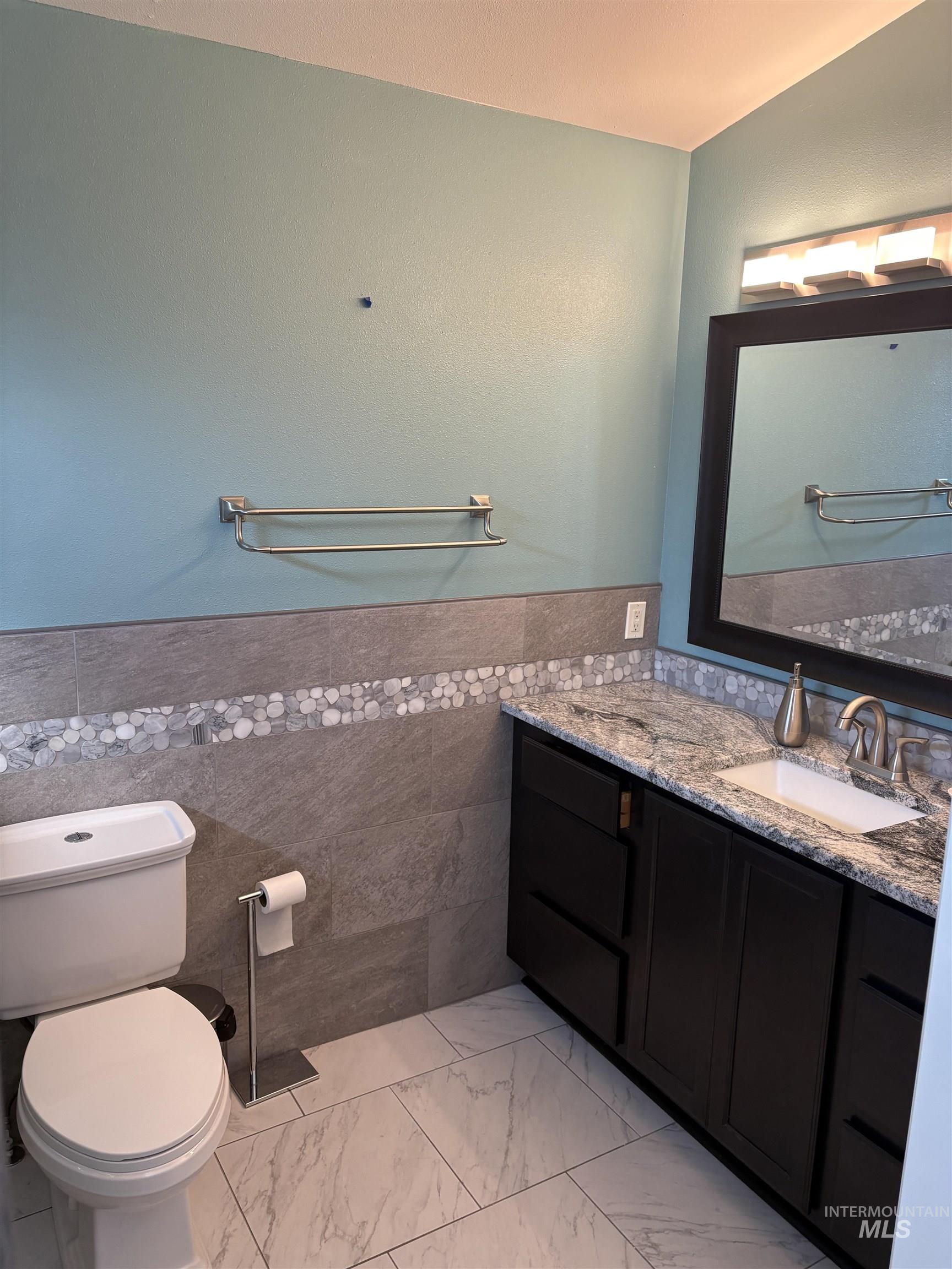 Half bath with tile walls, vanity, wainscoting, and light marble finish floors