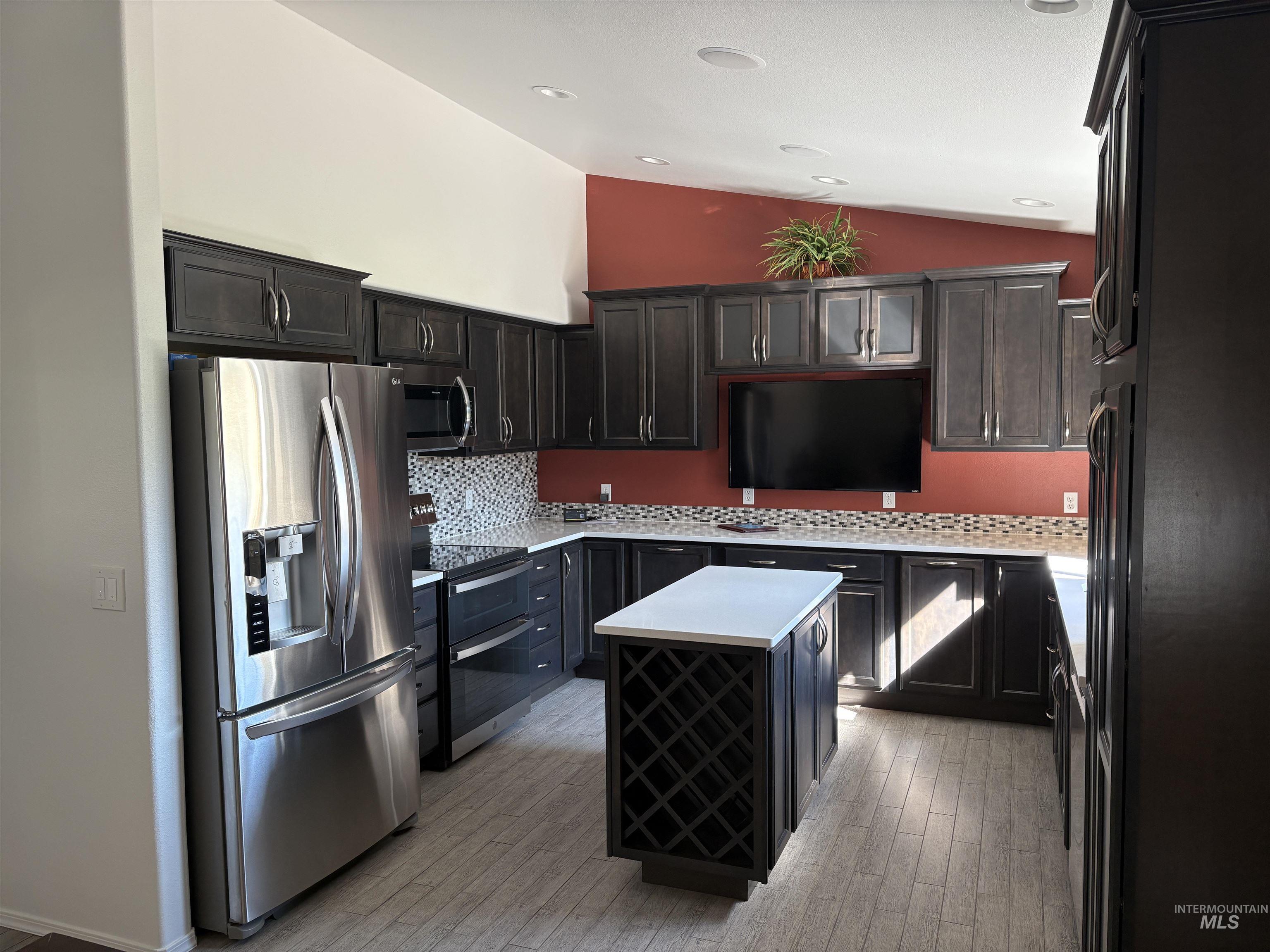 Kitchen with stainless steel appliances, backsplash, vaulted ceiling, a center island, and light wood finished floors