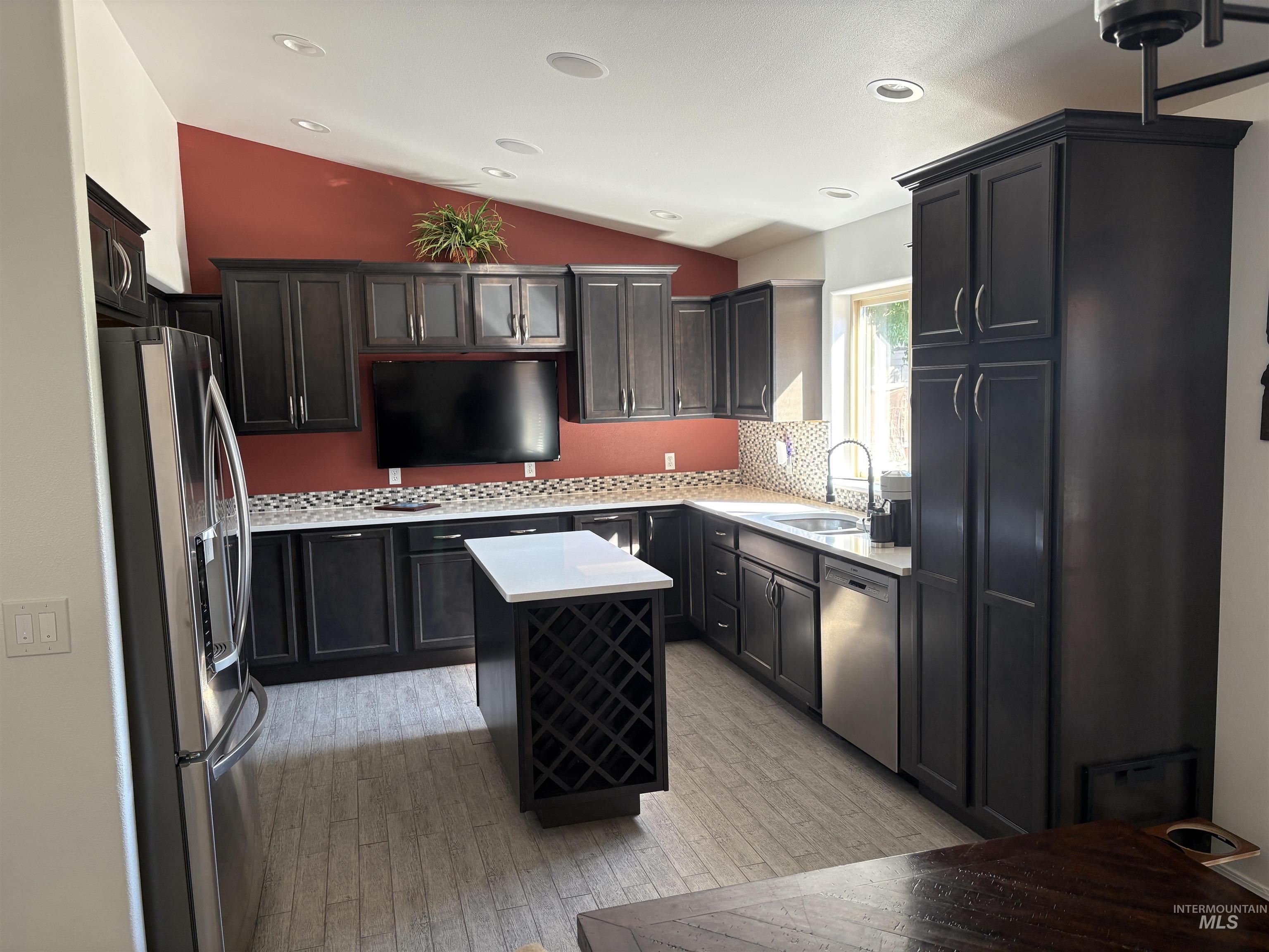 Kitchen with decorative backsplash, lofted ceiling, stainless steel appliances, light wood-type flooring, and a center island
