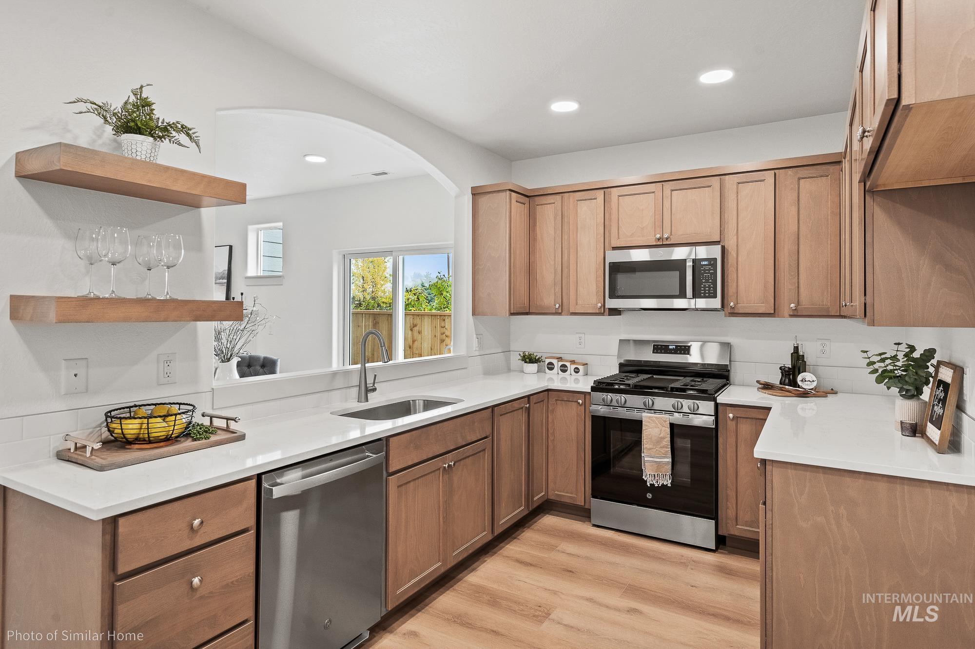 Kitchen with appliances with stainless steel finishes, light wood-type flooring, open shelves, light stone counters, and recessed lighting