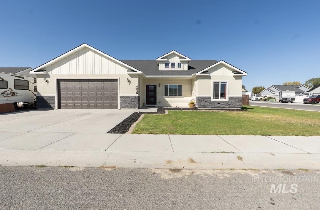 View of front of home featuring stone siding, a front yard, concrete driveway, board and batten siding, and a garage