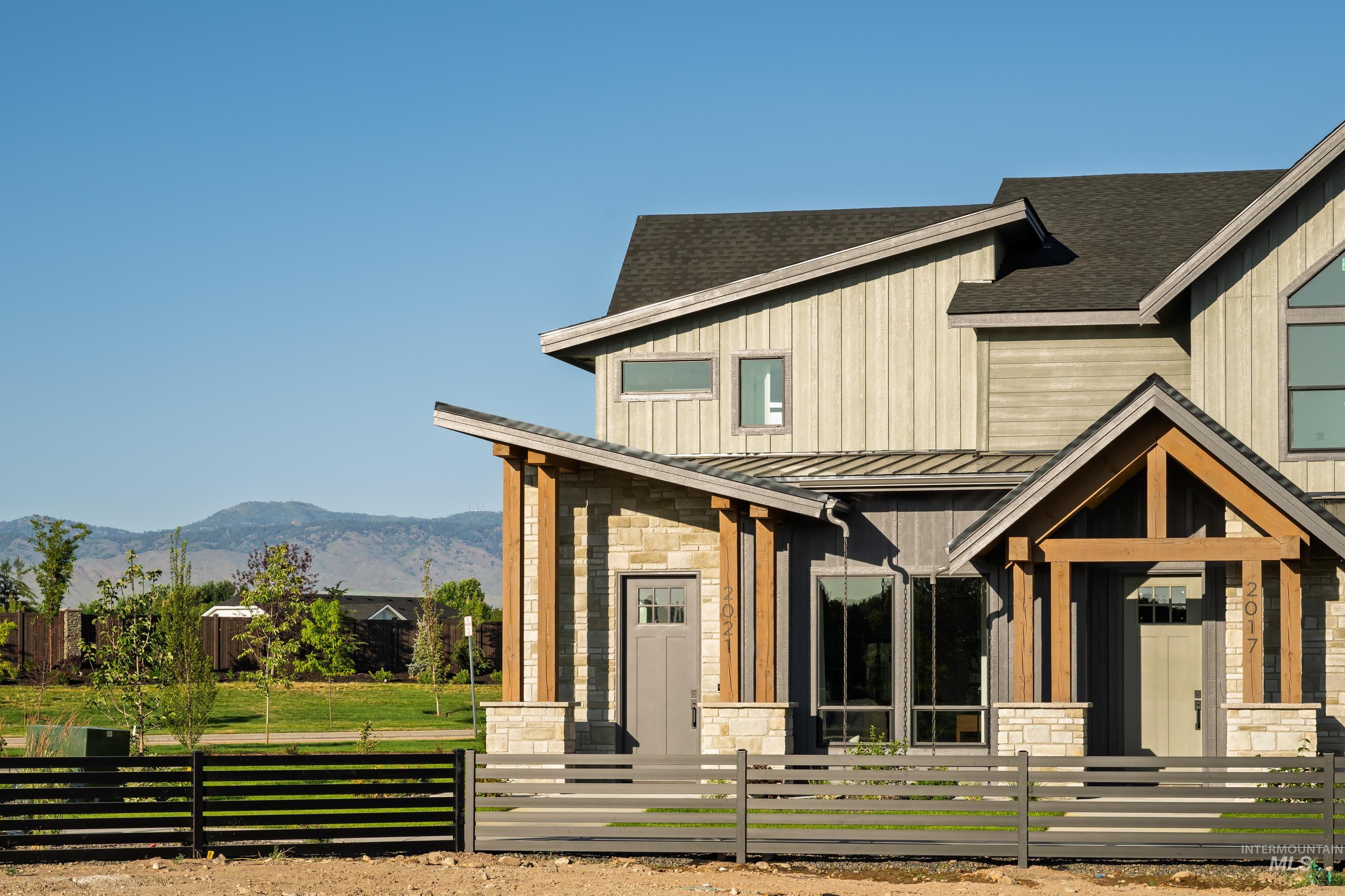 Modern farmhouse featuring stone siding, a standing seam roof, a metal roof, a fenced front yard, and a mountain view