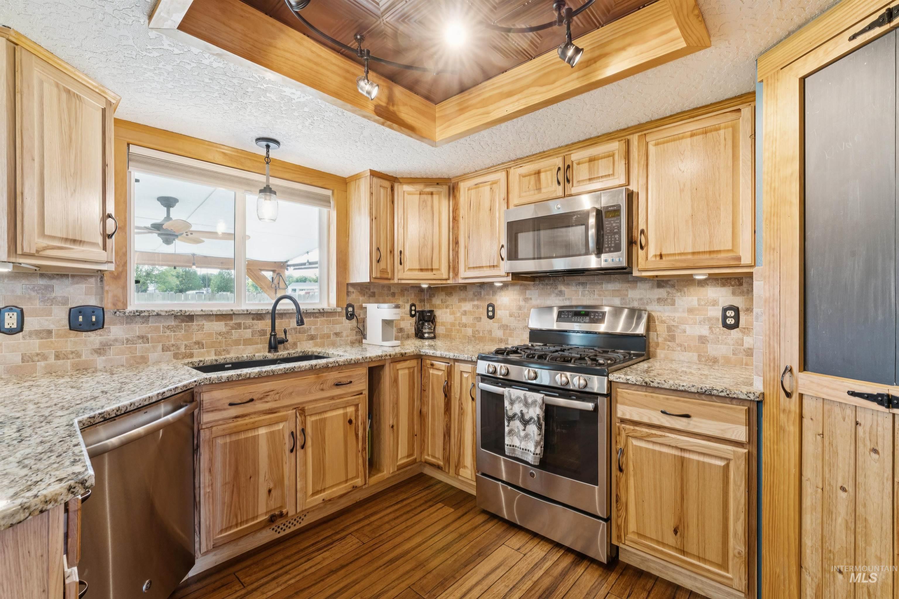 Kitchen featuring track lighting, stainless steel appliances, a raised ceiling, and backsplash