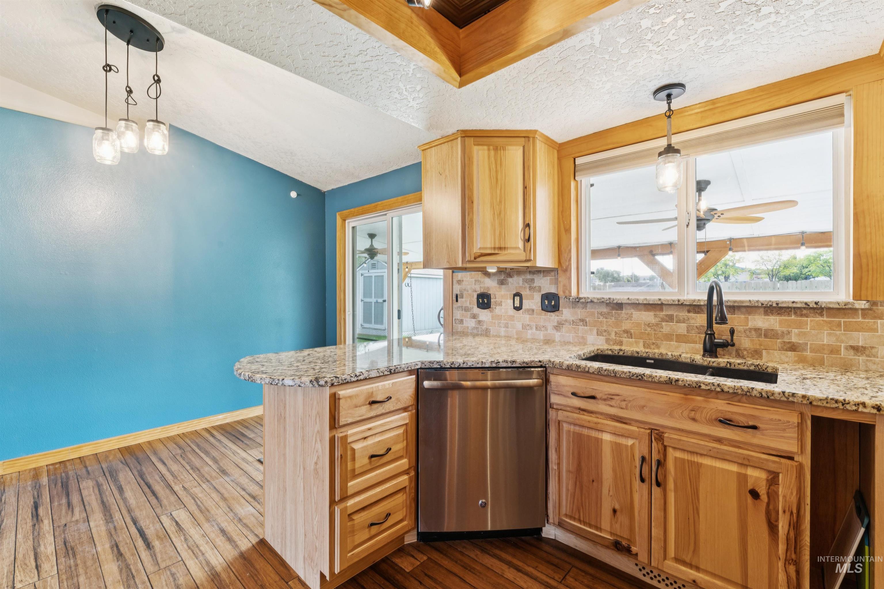 Kitchen with decorative light fixtures, dishwasher, backsplash, dark wood-type flooring, and light stone countertops