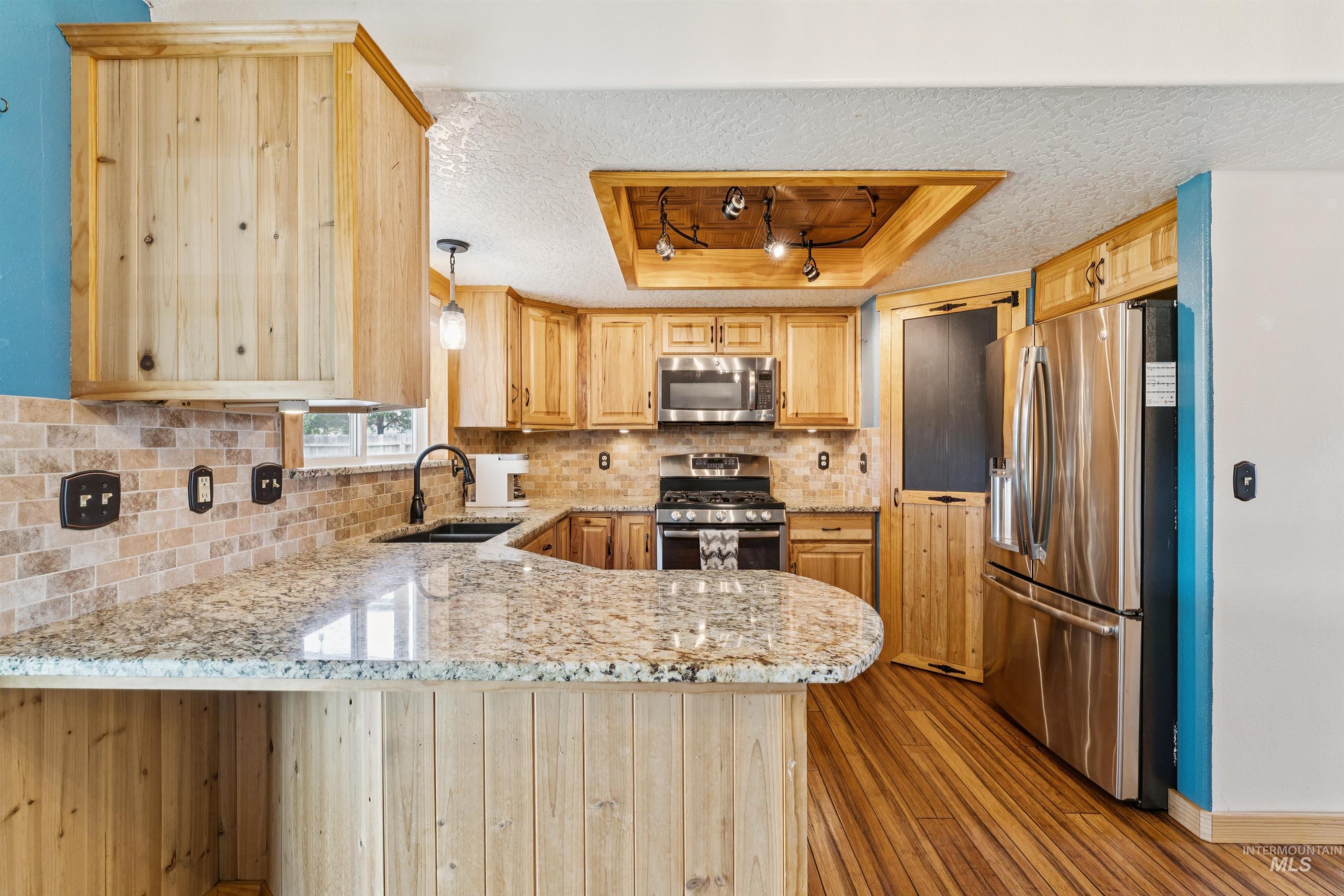 Kitchen featuring tasteful backsplash, rail lighting, appliances with stainless steel finishes, light stone countertops, and a peninsula