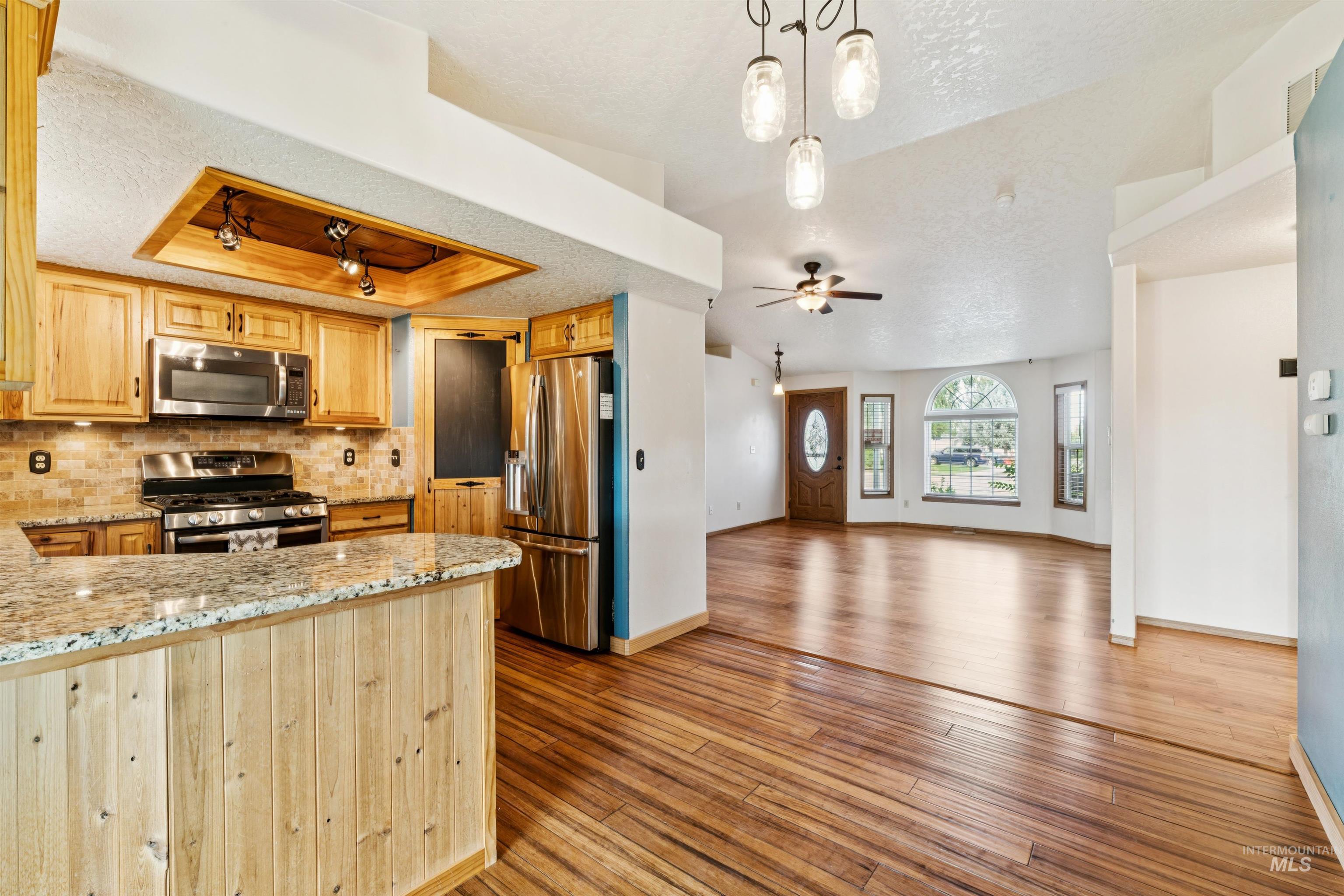 Kitchen with a textured ceiling, a tray ceiling, backsplash, appliances with stainless steel finishes, and light stone countertops