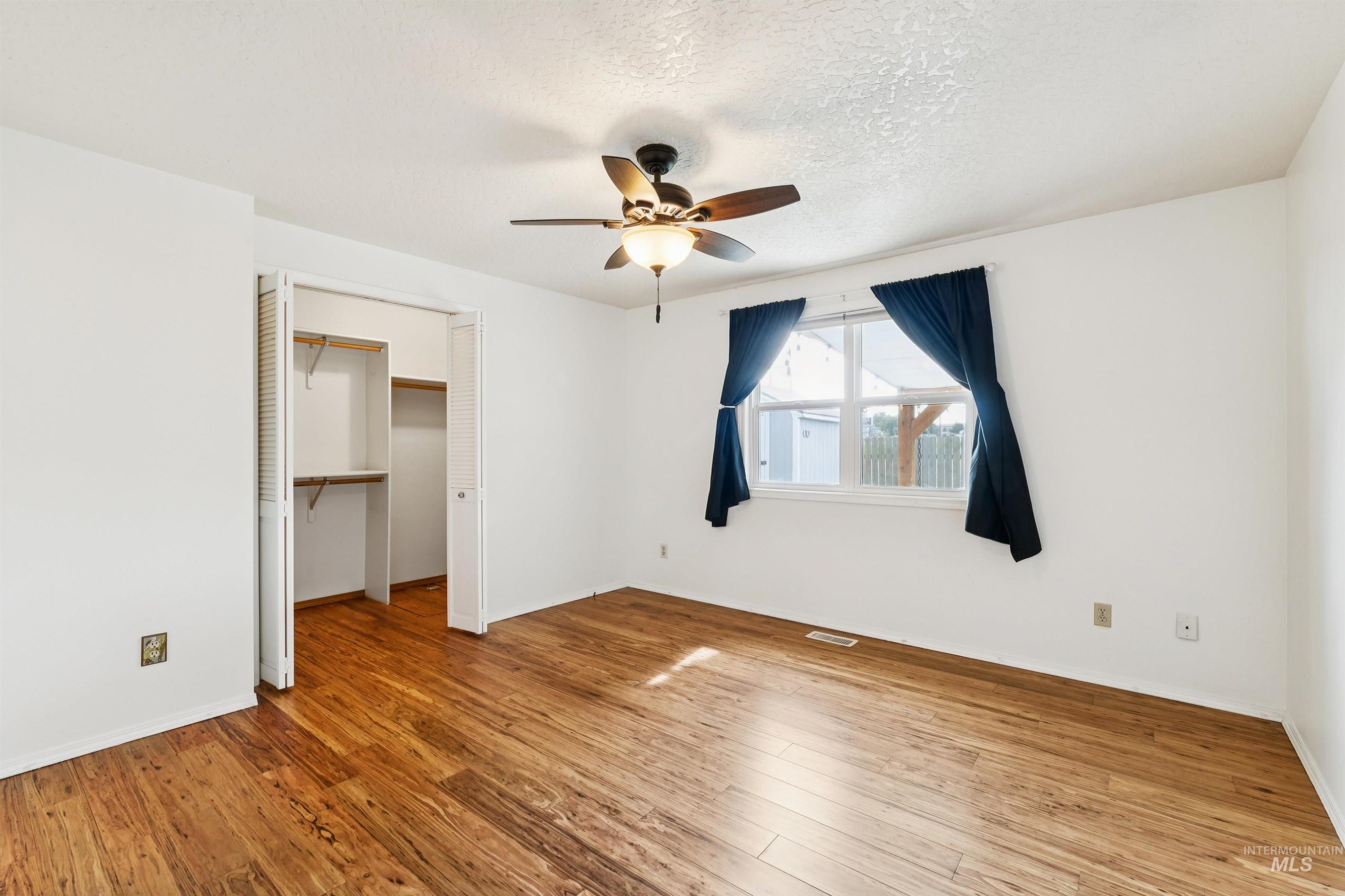 Unfurnished bedroom featuring a walk in closet, light wood-style flooring, ceiling fan, and a textured ceiling