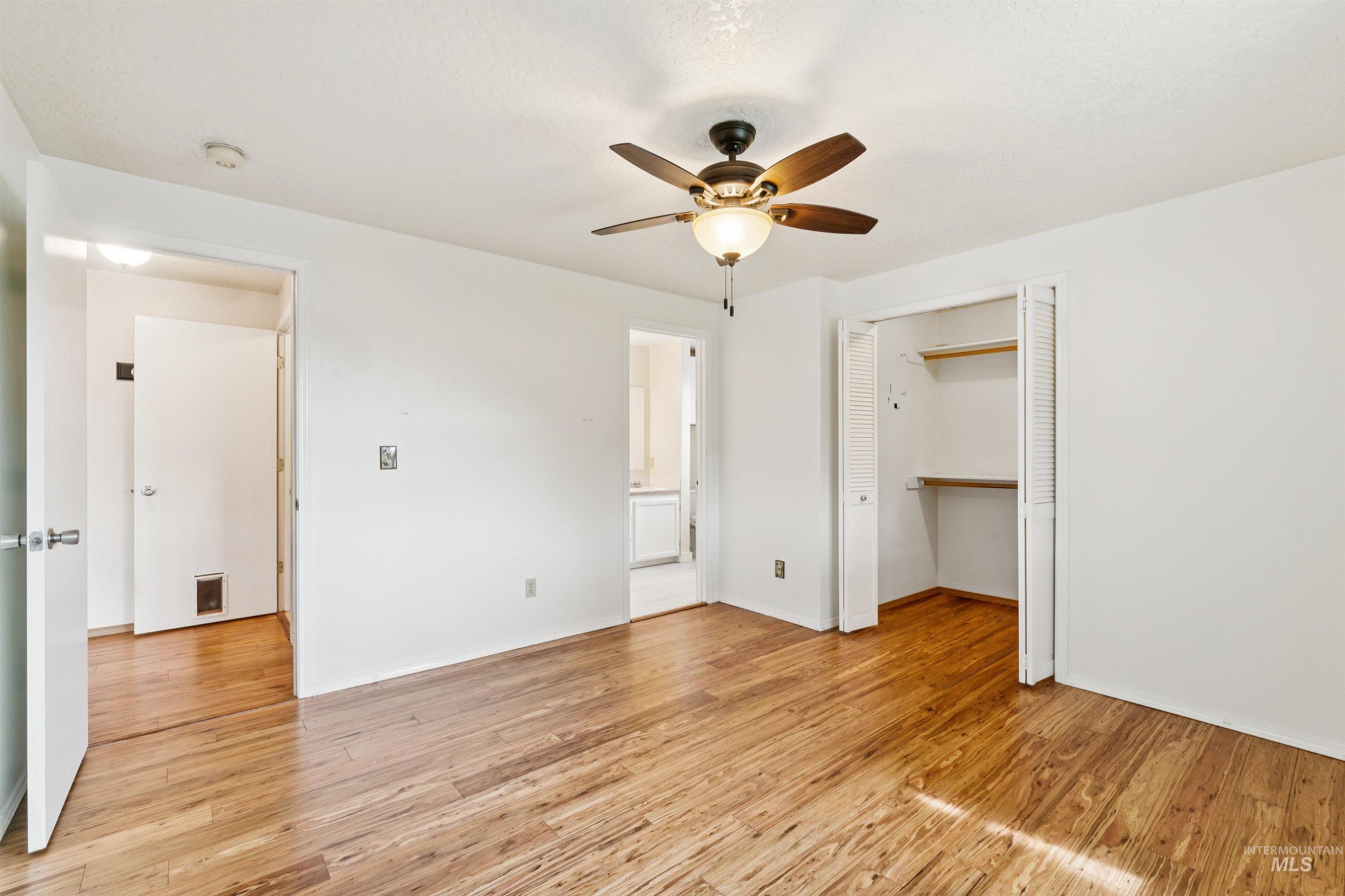 Unfurnished bedroom with light wood-style flooring, ceiling fan, ensuite bathroom, and a walk in closet