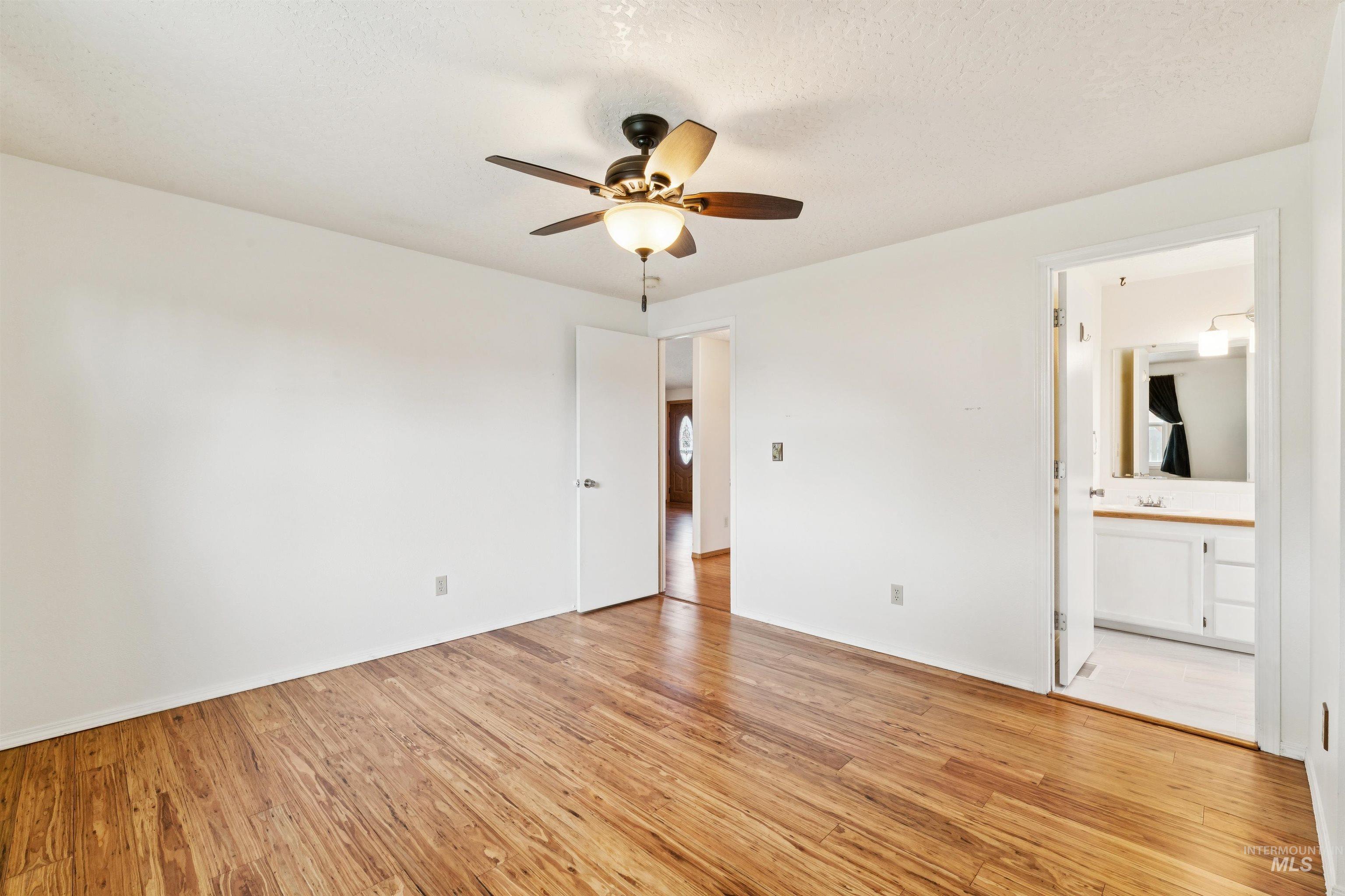 Main Unfurnished bedroom with light wood-style floors, ceiling fan, a textured ceiling, and ensuite bath