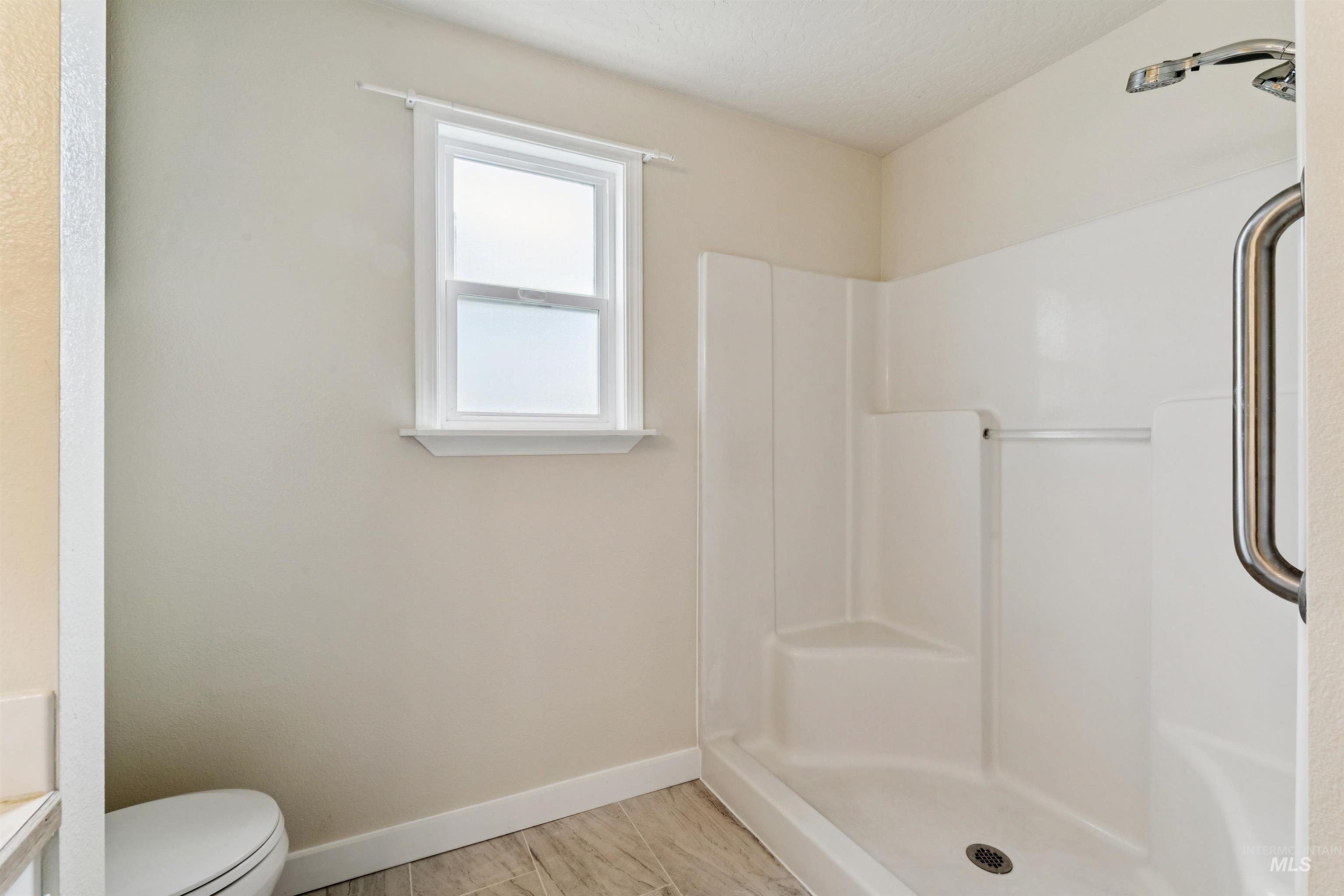 Full bath with a shower stall and baseboards