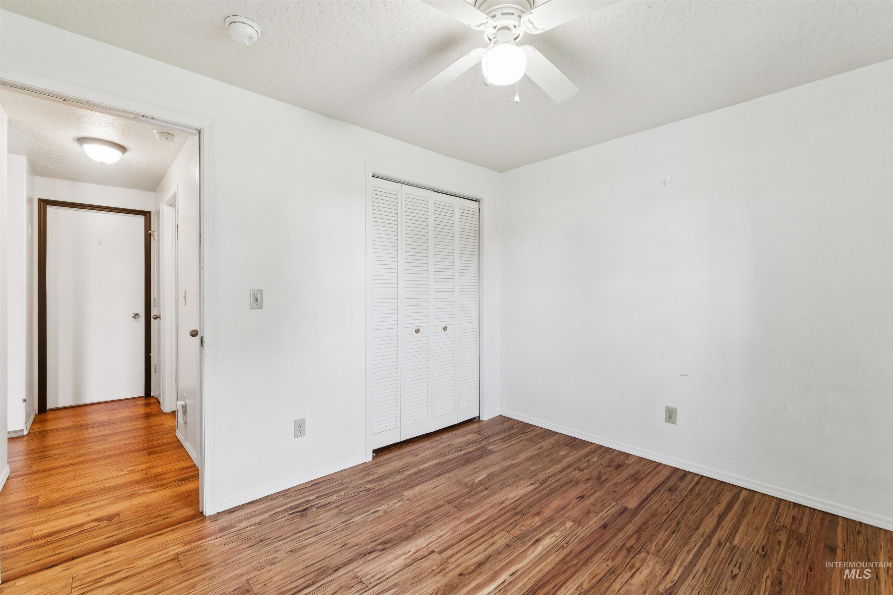 Unfurnished bedroom with wood finished floors, a closet, a textured ceiling, and a ceiling fan