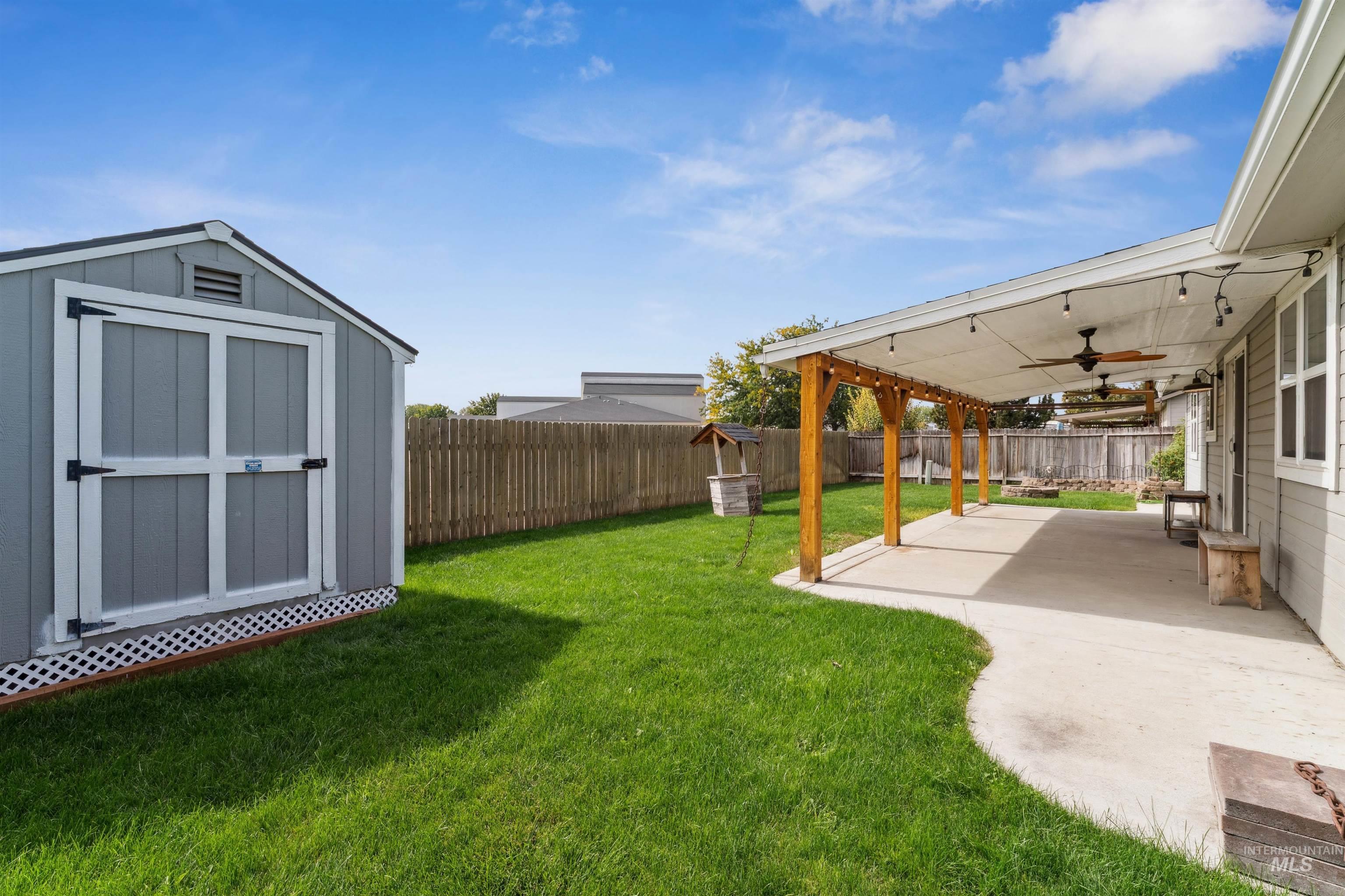 Fenced backyard with a patio, ceiling fan, and a storage unit