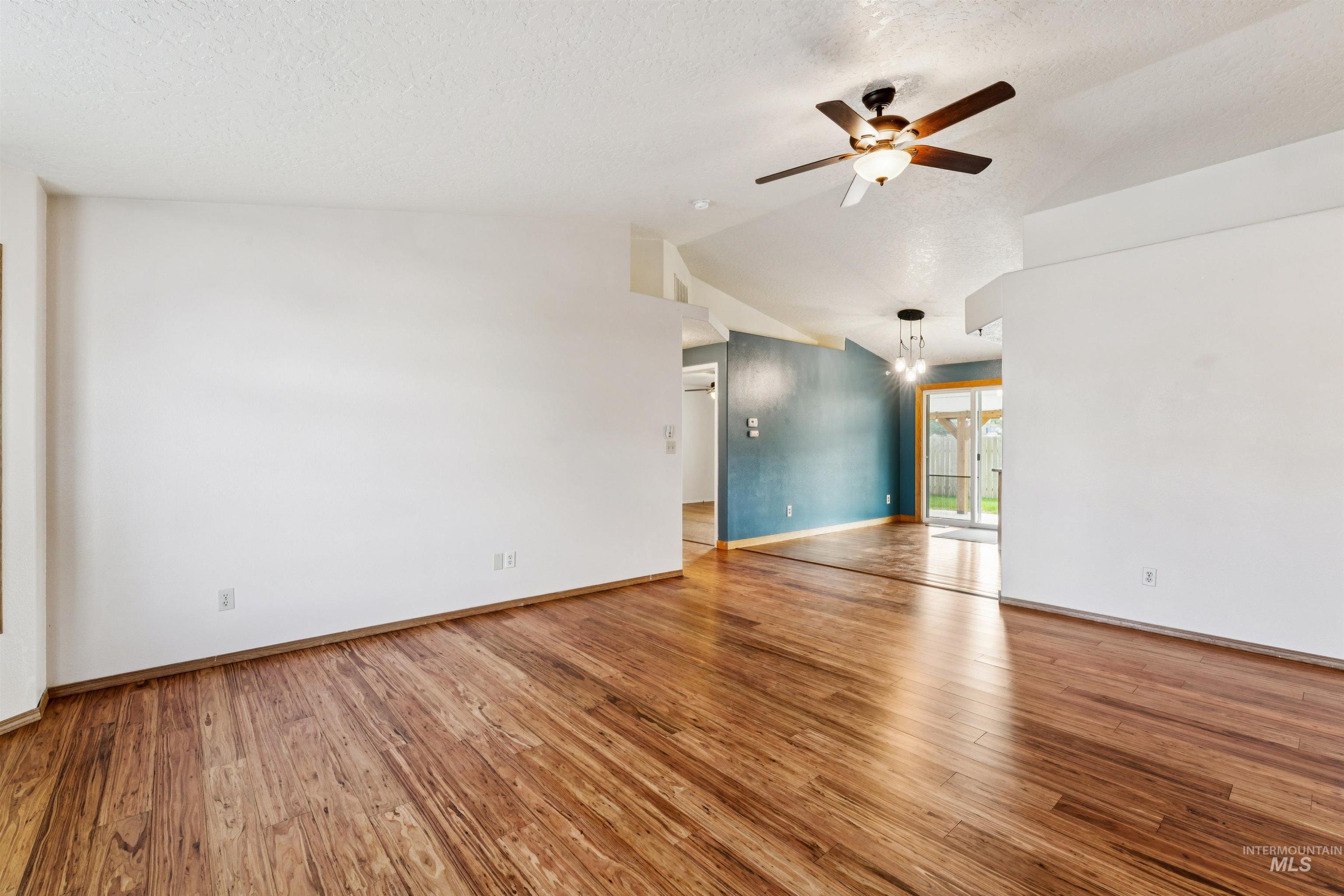 Empty room with light wood-style floors, ceiling fan, a textured ceiling, and lofted ceiling