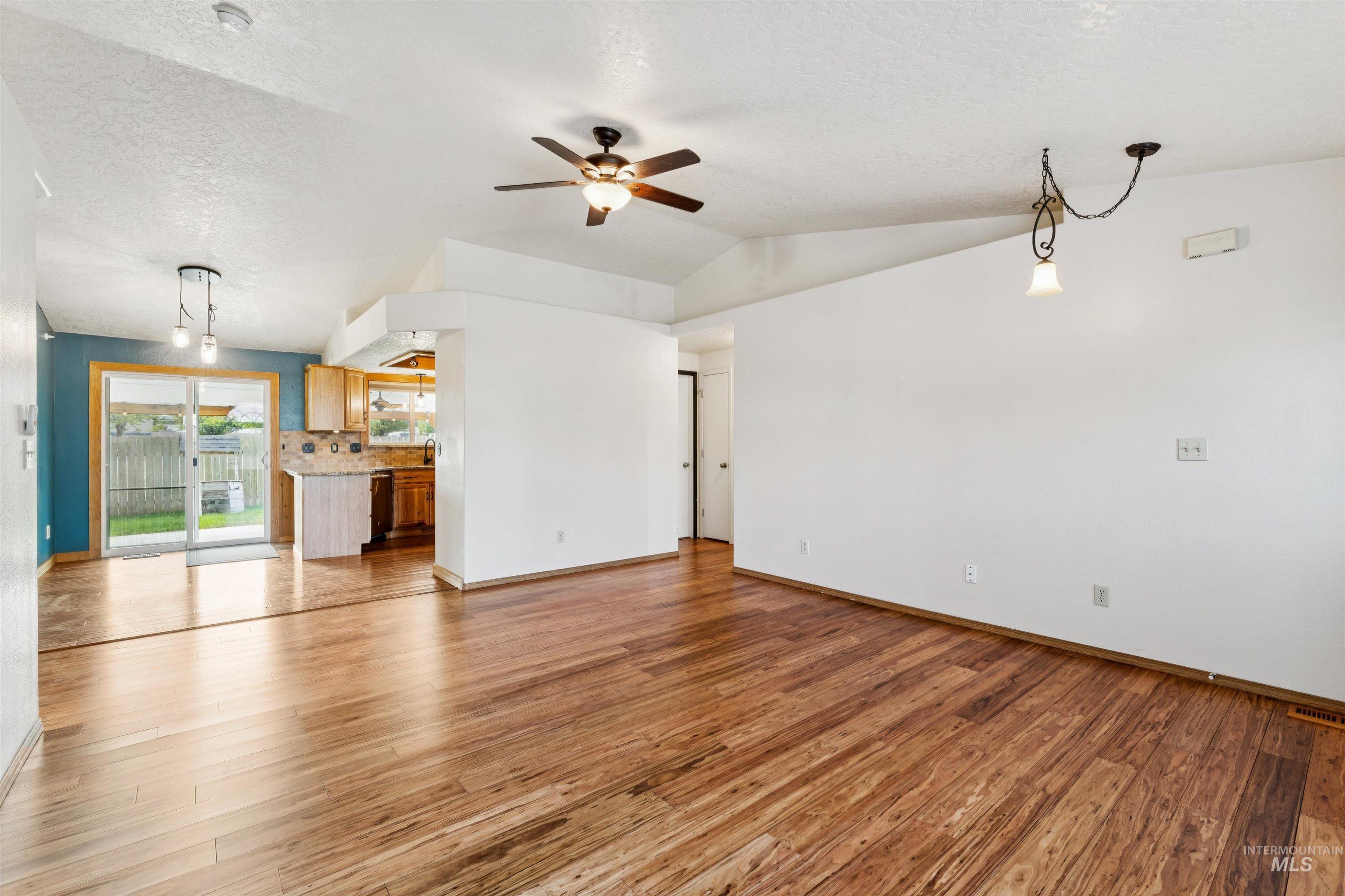 Unfurnished living room featuring light wood-style flooring, a textured ceiling, a ceiling fan, and lofted ceiling