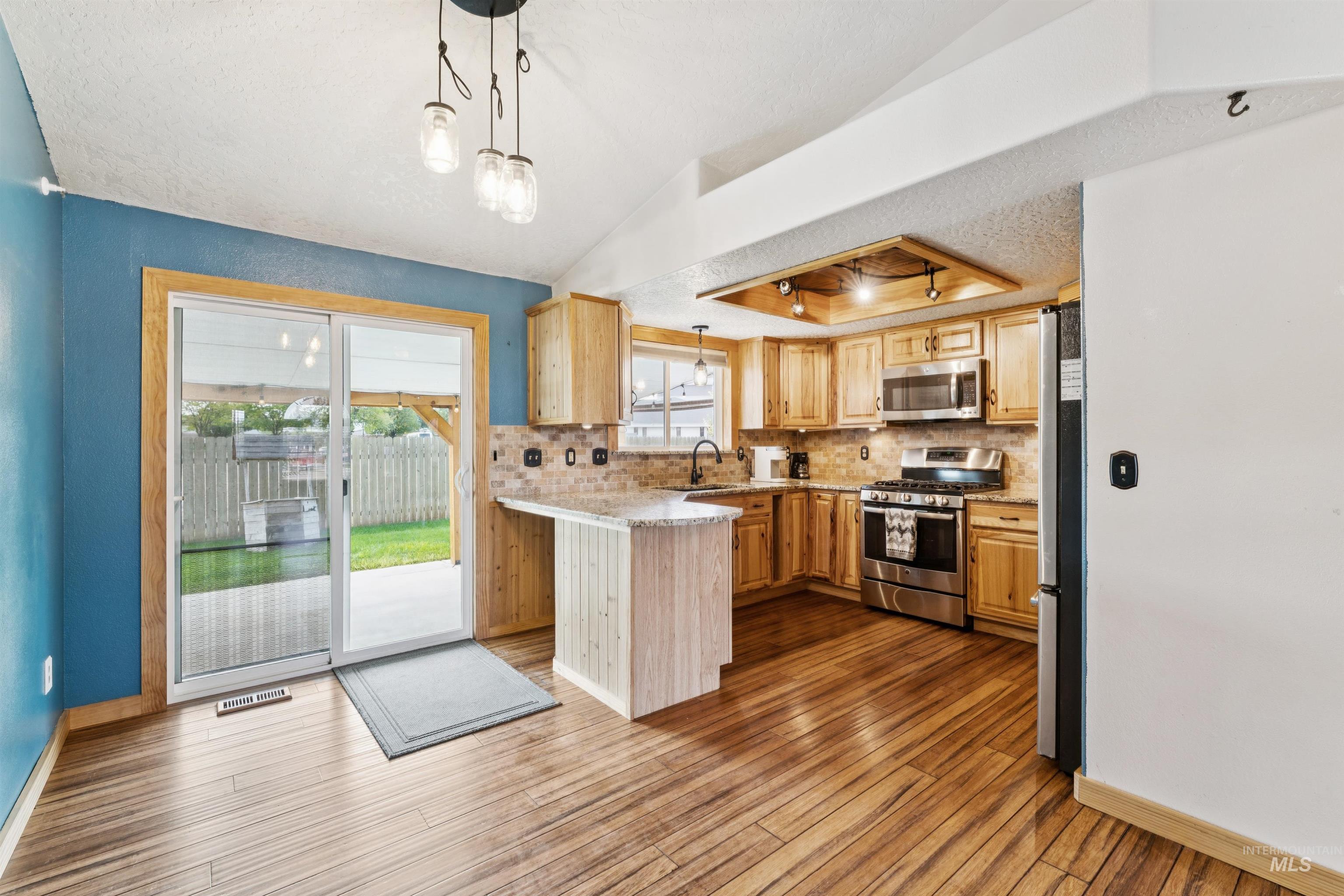 Kitchen featuring decorative light fixtures, backsplash, a textured ceiling, stainless steel appliances, and a tray ceiling