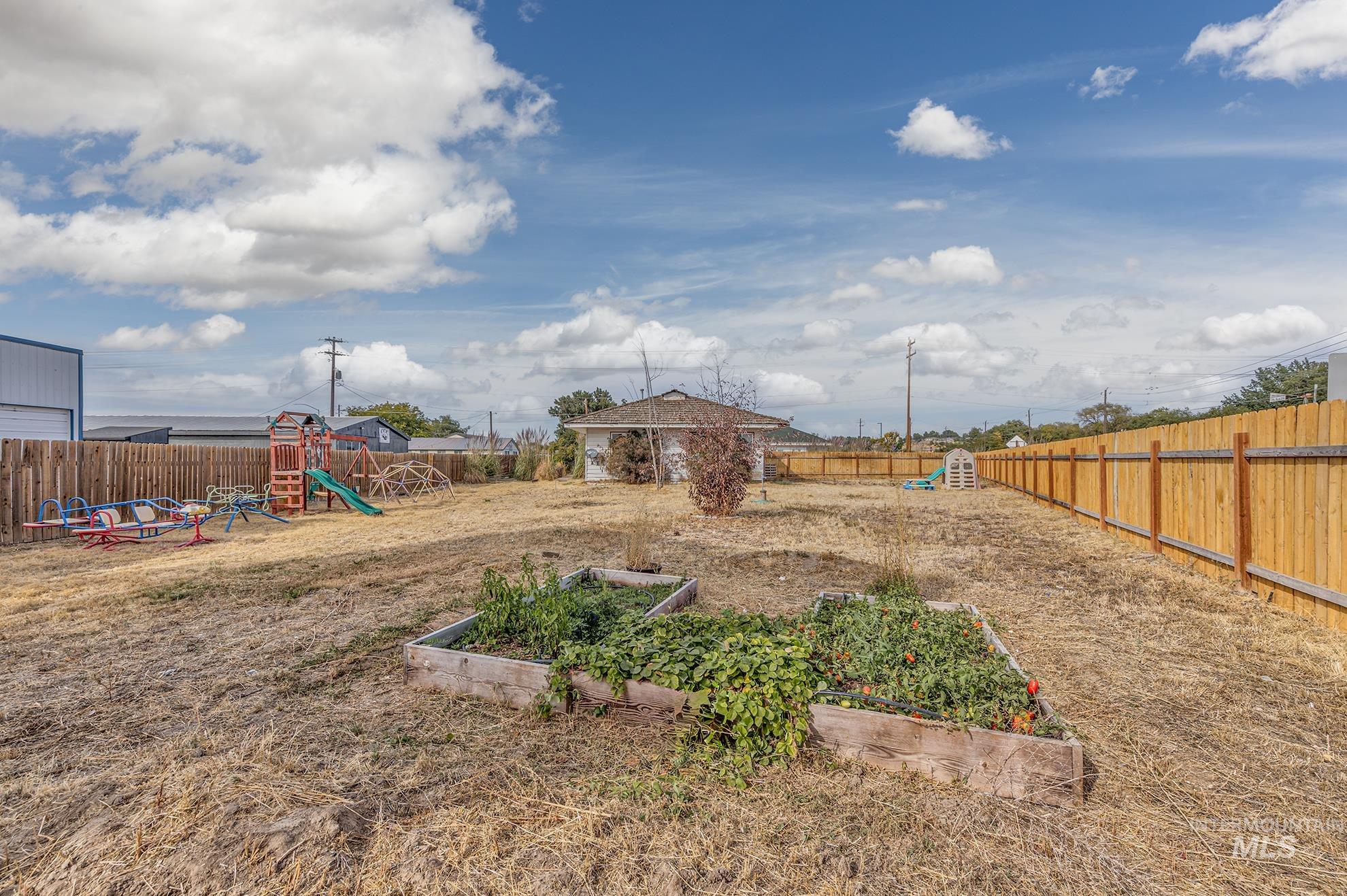 Fenced backyard with a playground and a vegetable garden