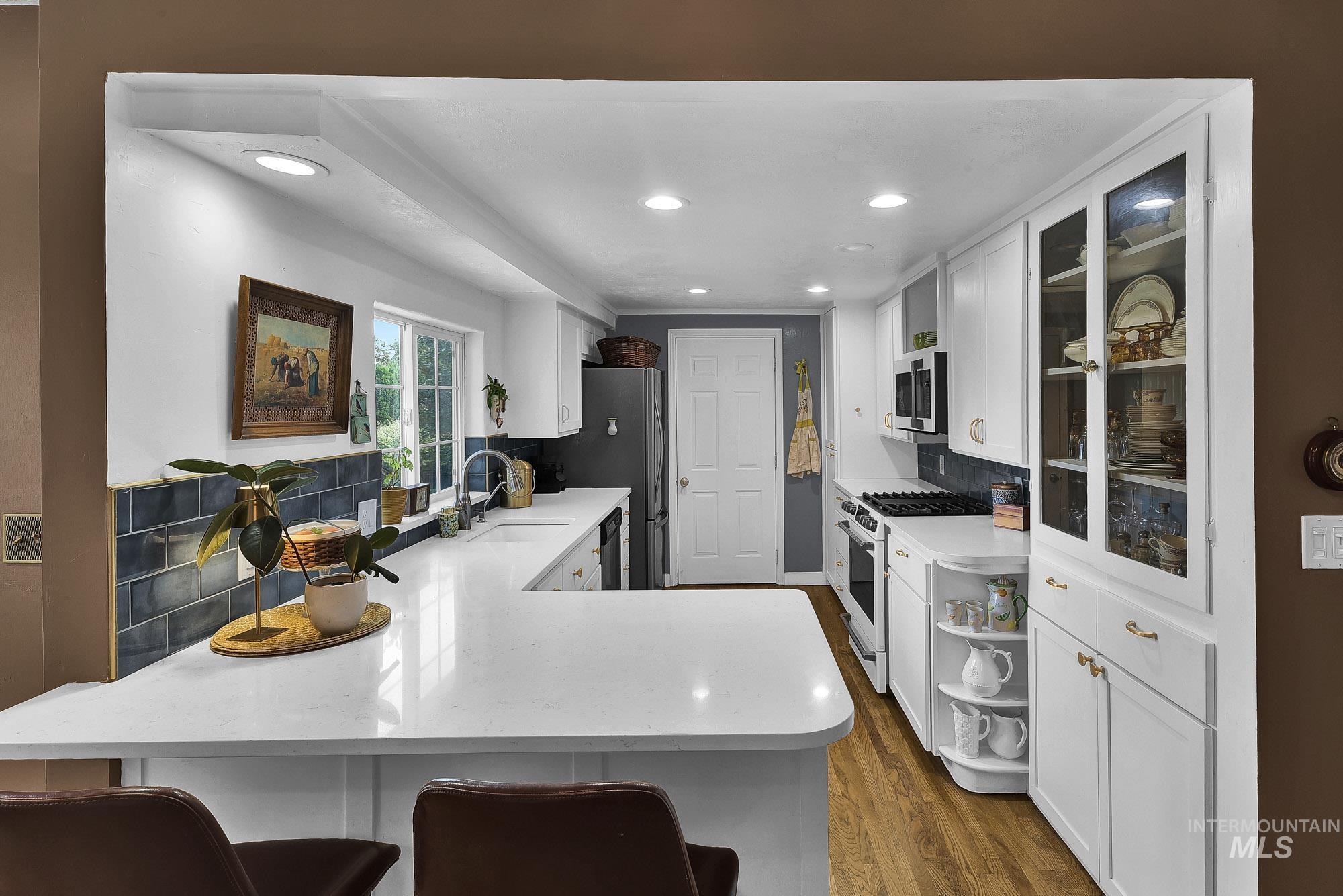 Kitchen featuring white cabinets, backsplash, hardwood floors, a breakfast bar and recessed lighting