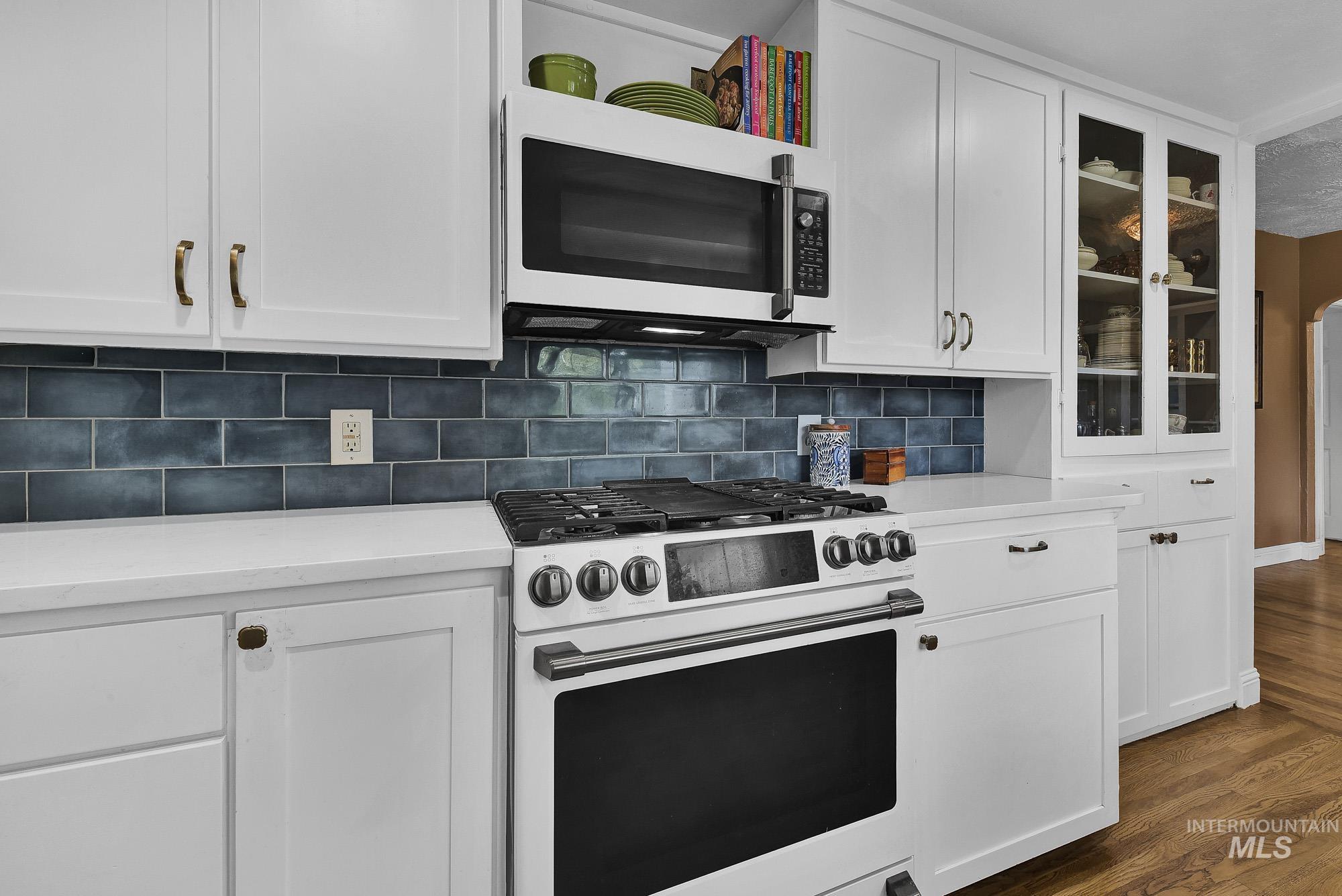 Kitchen featuring white cabinetry, GE Cafe series white appliances, backsplash, glass insert cabinets, and hard wood flooring