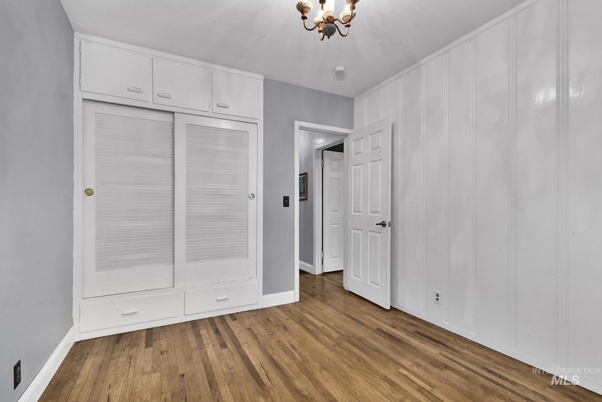 Unfurnished bedroom featuring wood finished floors, a chandelier, a closet, and a decorative wall