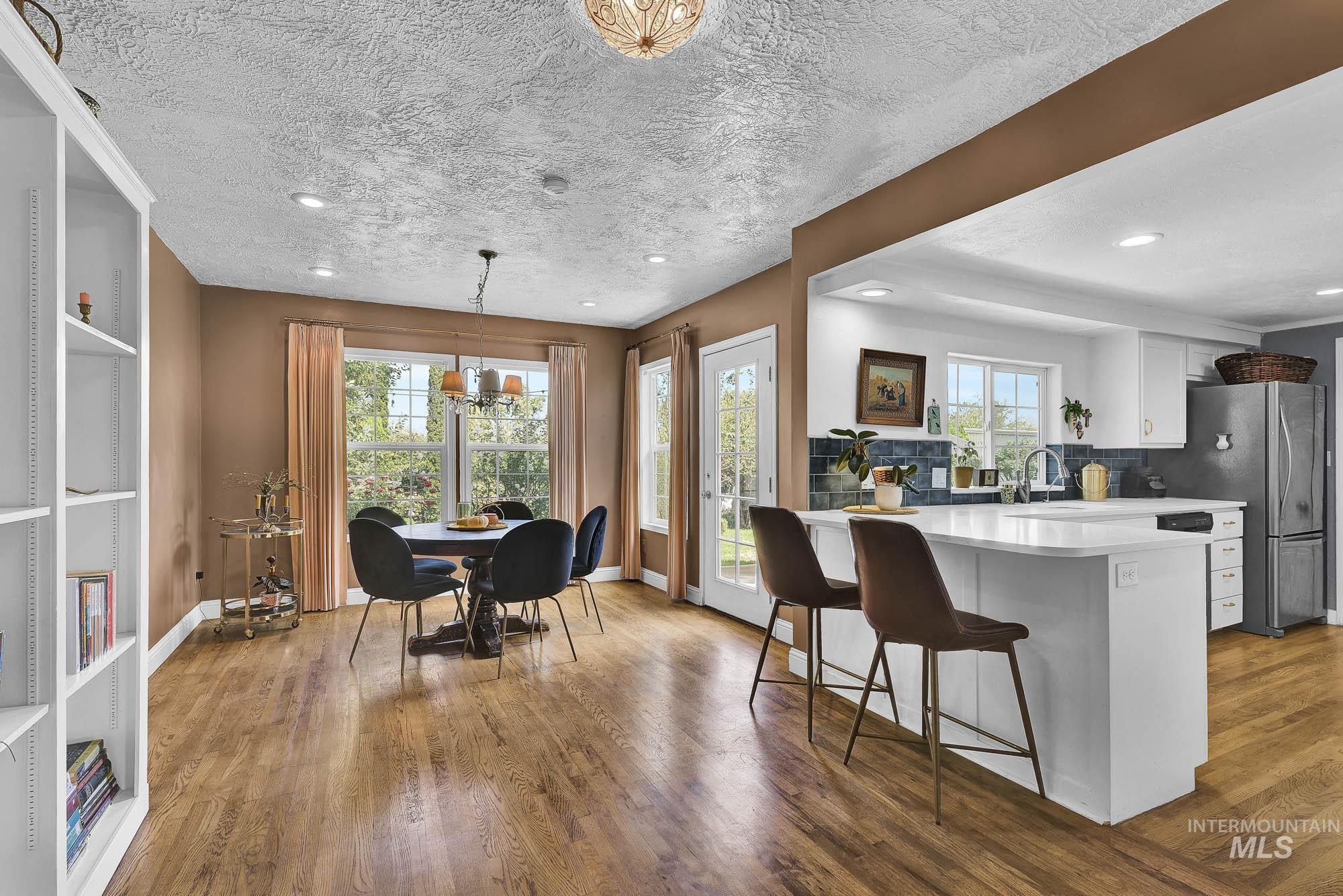 Kitchen /Dining area with wood finished floors, a breakfast bar area, white cabinets and full tile backsplash