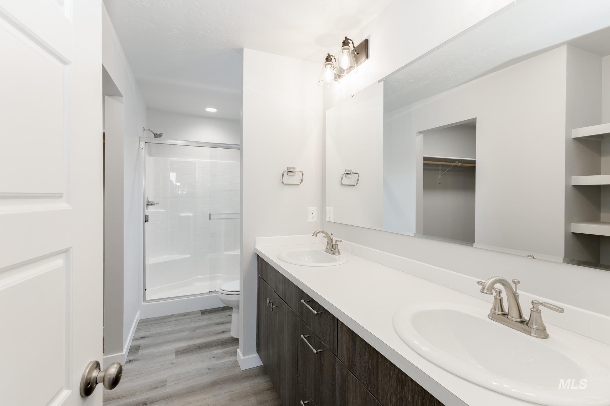 Full bathroom featuring a shower stall, double vanity, wood finished floors, and recessed lighting