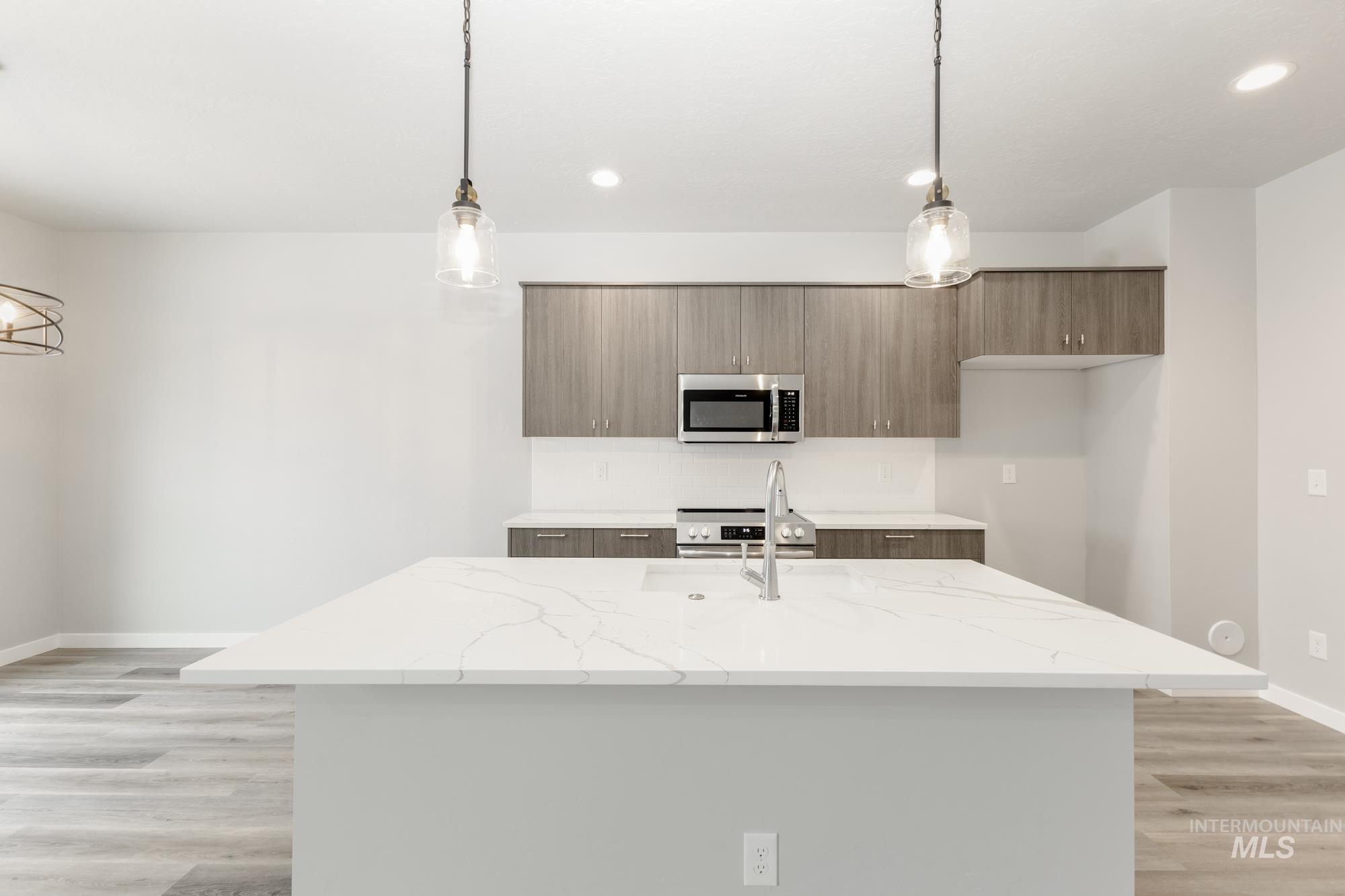 Kitchen featuring stainless steel appliances, pendant lighting, an island with sink, light wood-style floors, and recessed lighting