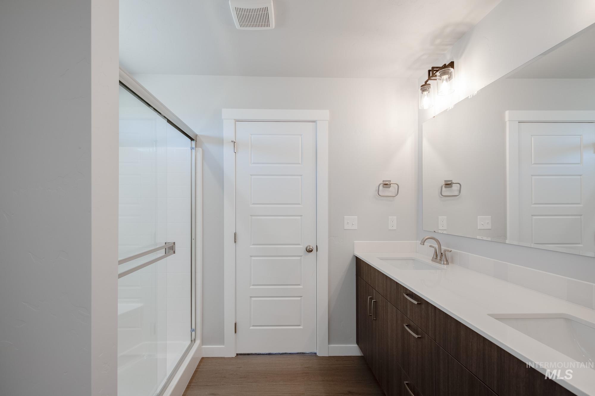 Full bath with a stall shower, dark wood-style flooring, and double vanity