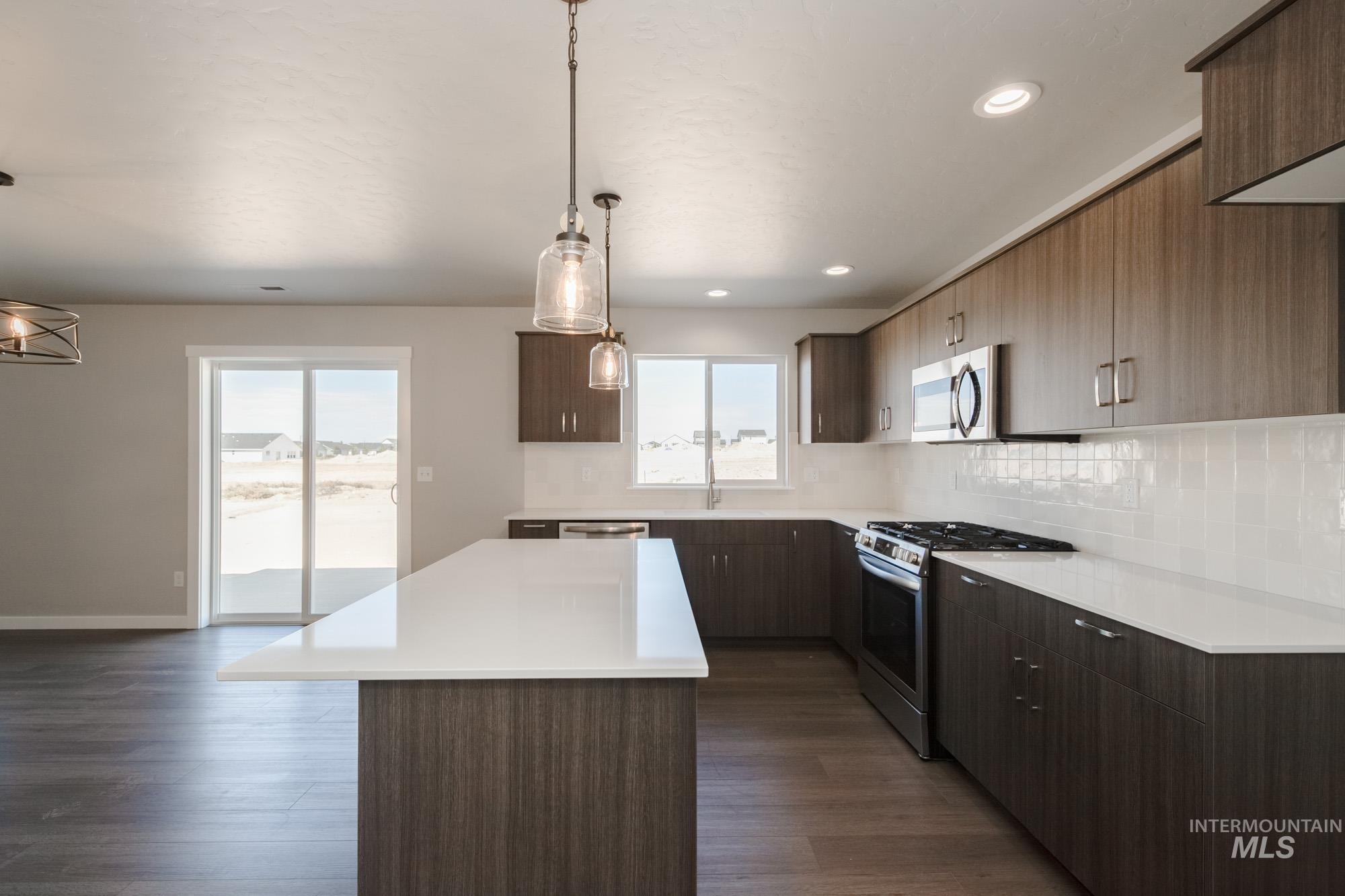 Kitchen featuring appliances with stainless steel finishes, decorative backsplash, pendant lighting, a kitchen island, and dark wood-style floors