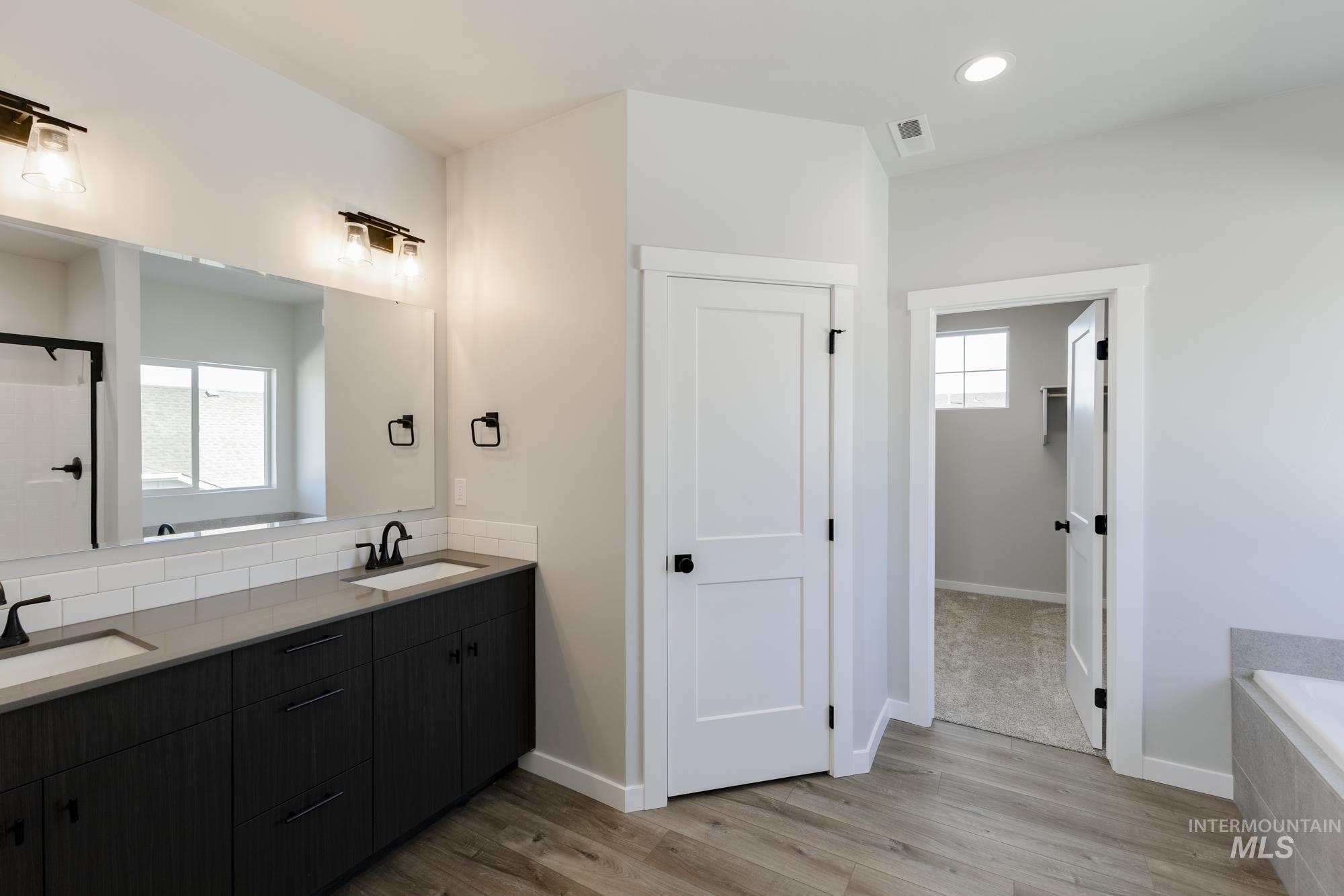 Bathroom with double vanity, a garden tub, light wood-style flooring, recessed lighting, and a shower
