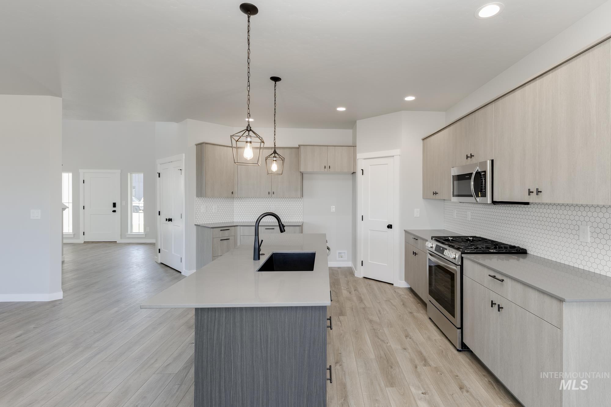 Kitchen featuring appliances with stainless steel finishes, hanging light fixtures, light wood-type flooring, modern cabinets, and an island with sink