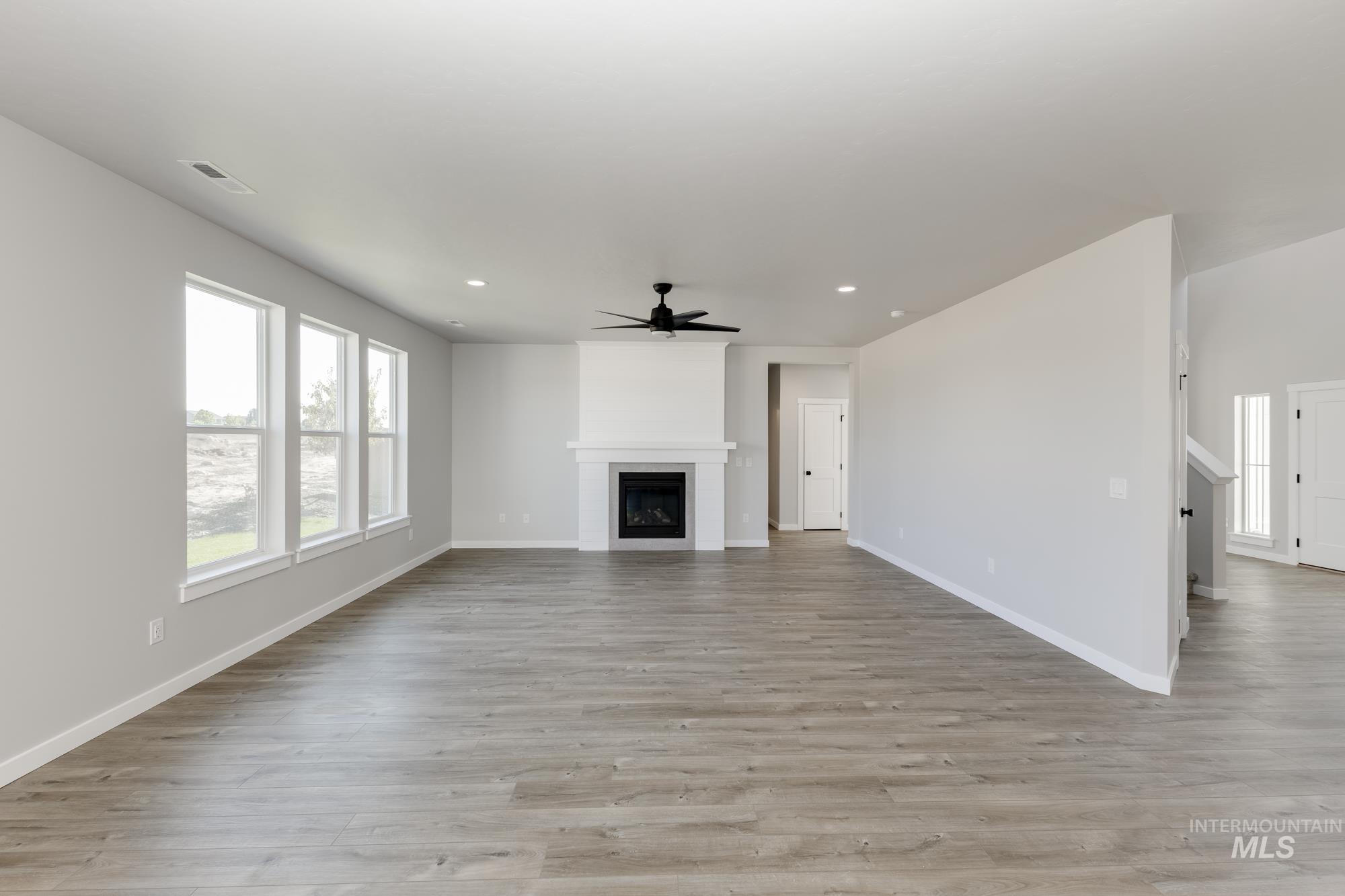 Unfurnished living room featuring a large fireplace, light wood-style flooring, a ceiling fan, and recessed lighting