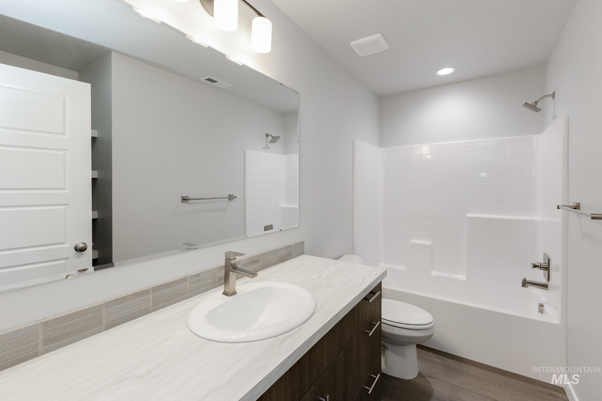 Full bathroom with washtub / shower combination, vanity, dark wood-type flooring, and recessed lighting