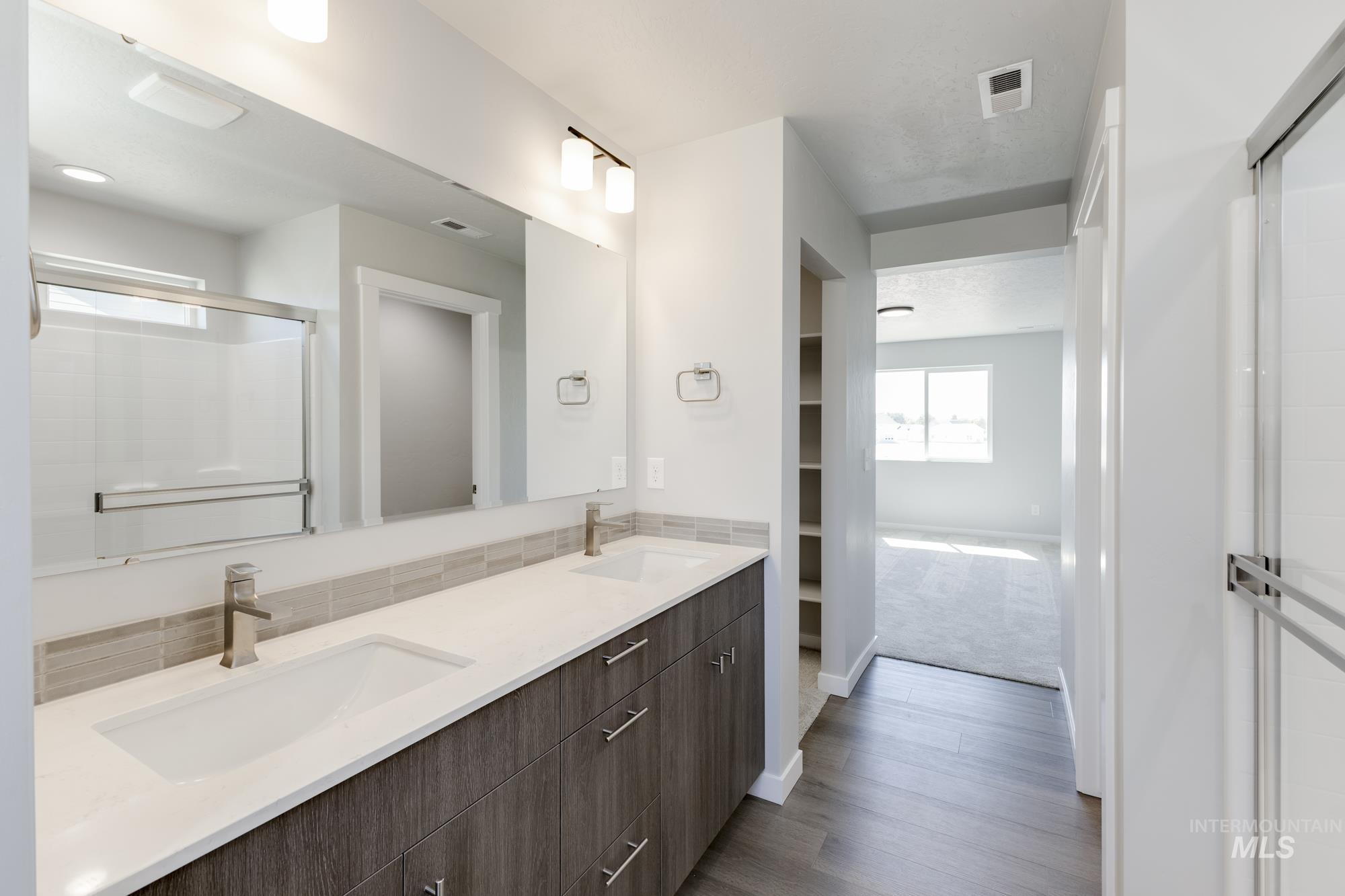 Bathroom with double vanity, a stall shower, and dark wood finished floors