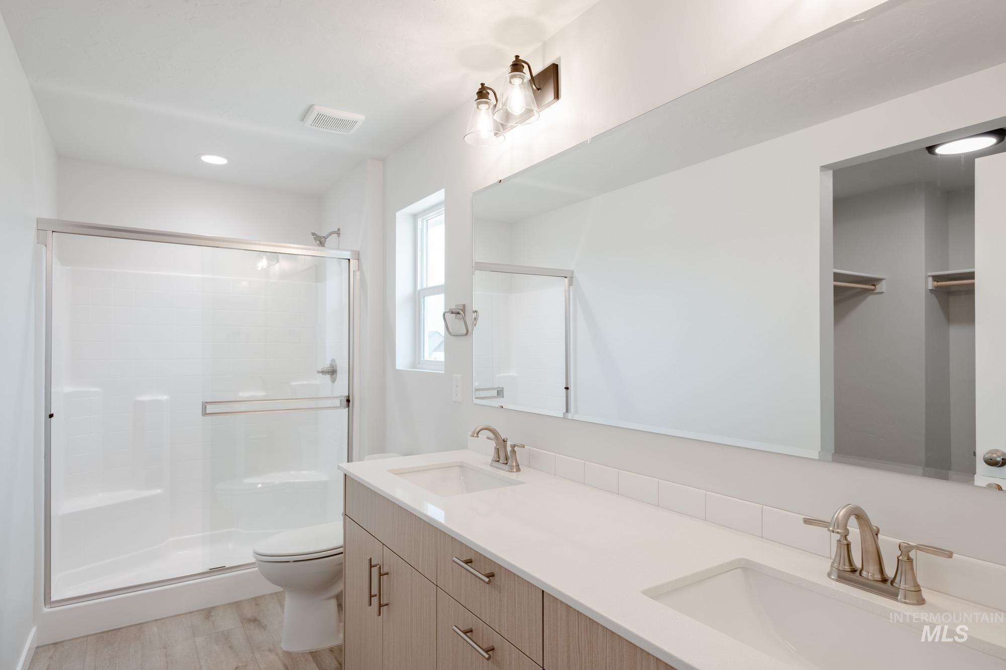 Full bath with a shower stall, light wood finished floors, double vanity, recessed lighting, and a closet