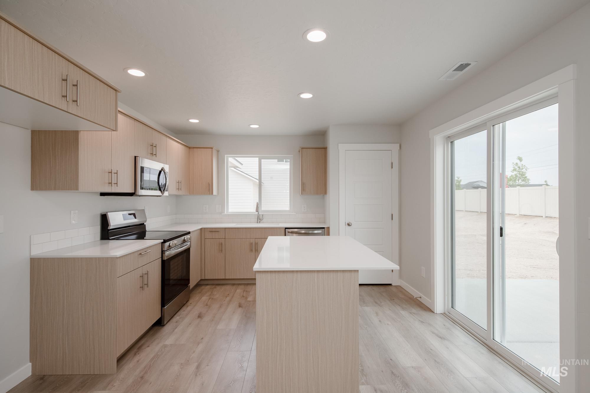 Kitchen featuring light brown cabinets, stainless steel appliances, recessed lighting, modern cabinets, and light wood-style floors