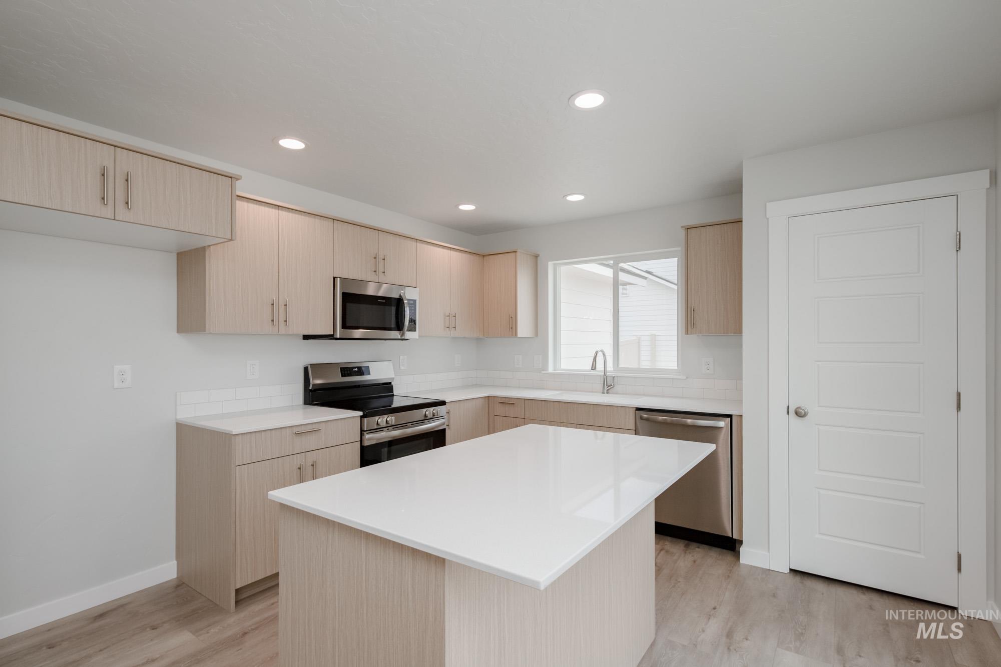 Kitchen featuring stainless steel appliances, light brown cabinetry, light wood finished floors, recessed lighting, and a kitchen island