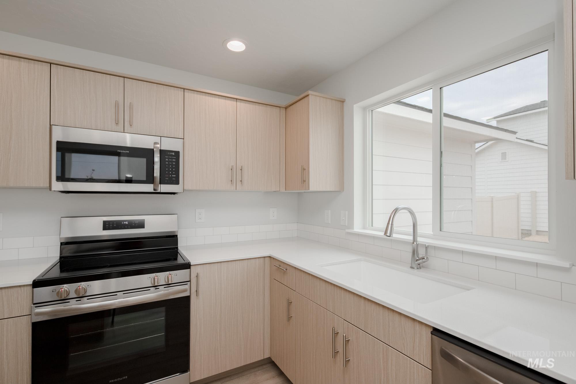 Kitchen with light brown cabinets, stainless steel appliances, recessed lighting, and light stone counters