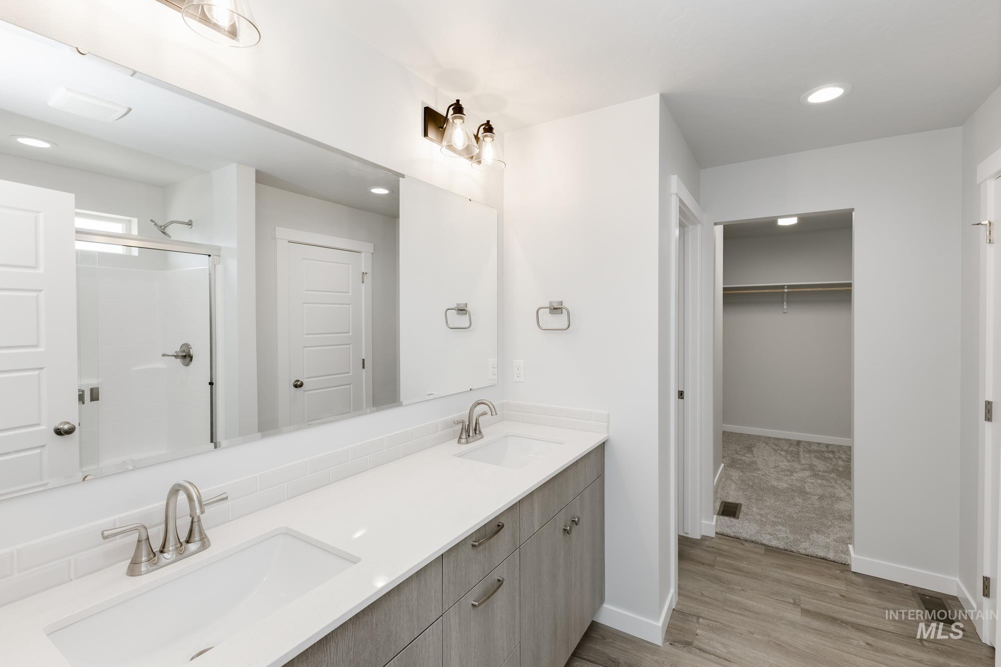 Full bathroom with recessed lighting, double vanity, wood finished floors, a spacious closet, and an enclosed shower