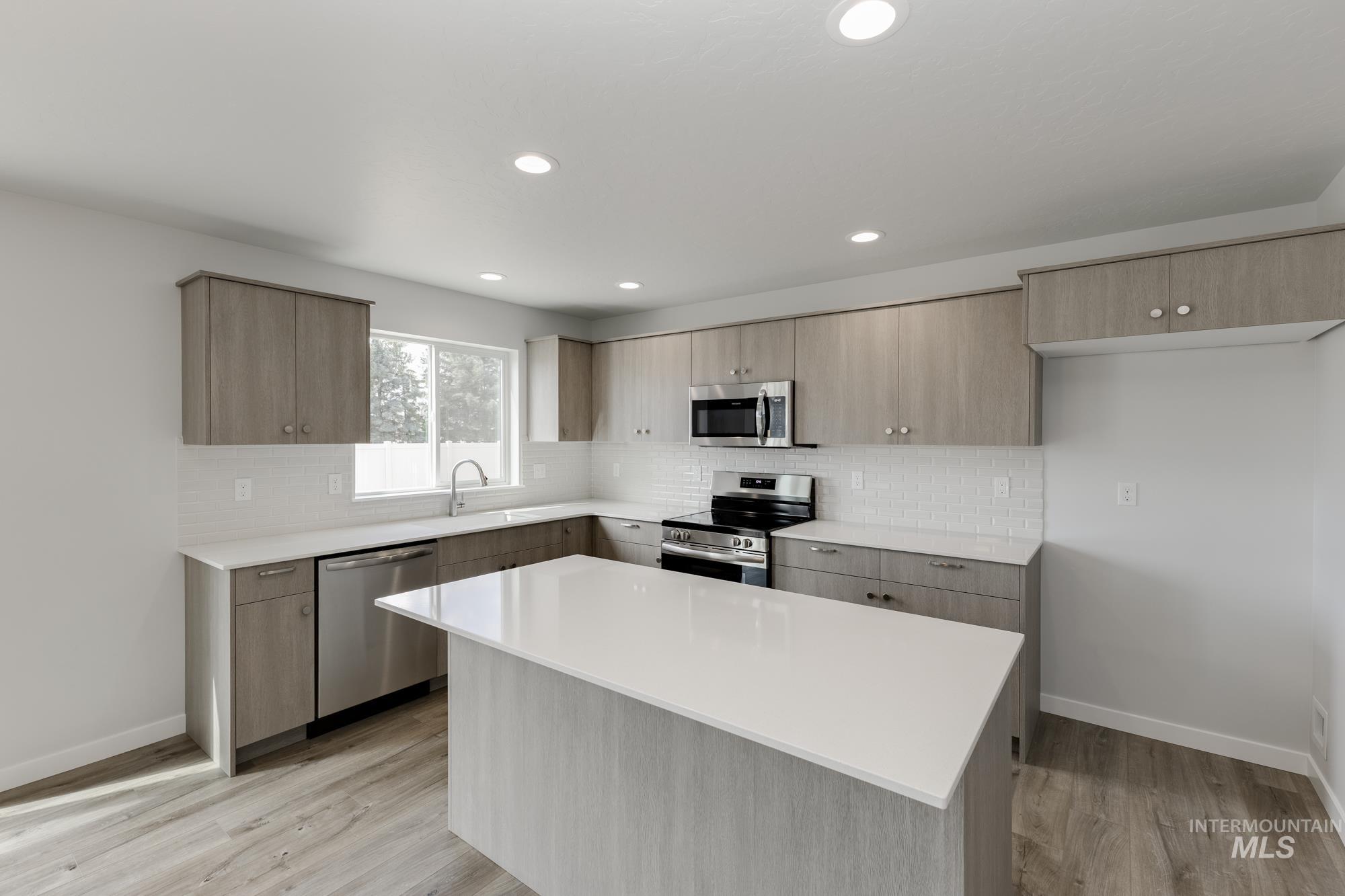 Kitchen featuring appliances with stainless steel finishes, light countertops, tasteful backsplash, light wood-type flooring, and recessed lighting