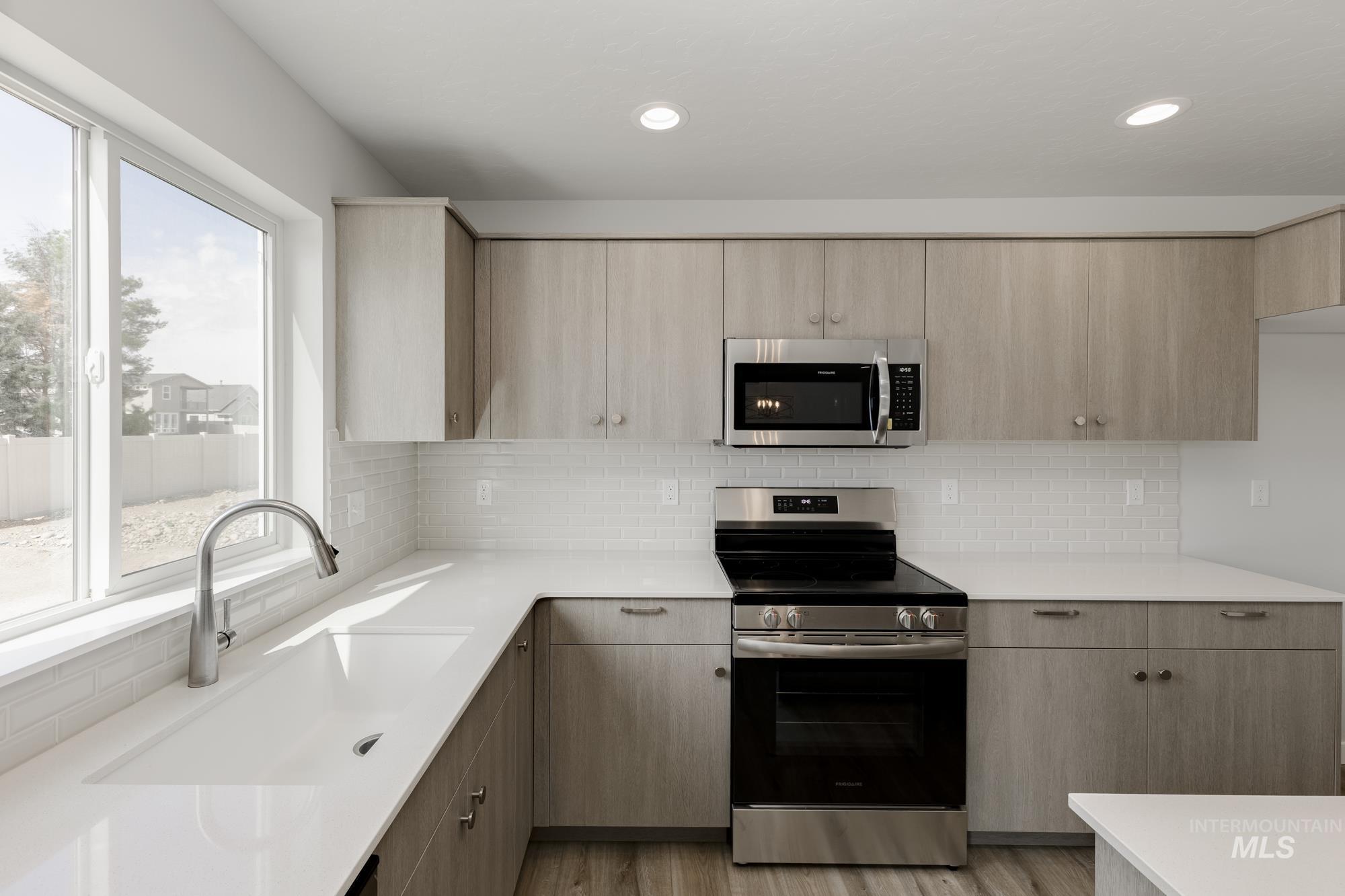 Kitchen featuring appliances with stainless steel finishes, light countertops, light brown cabinetry, modern cabinets, and light wood-style floors